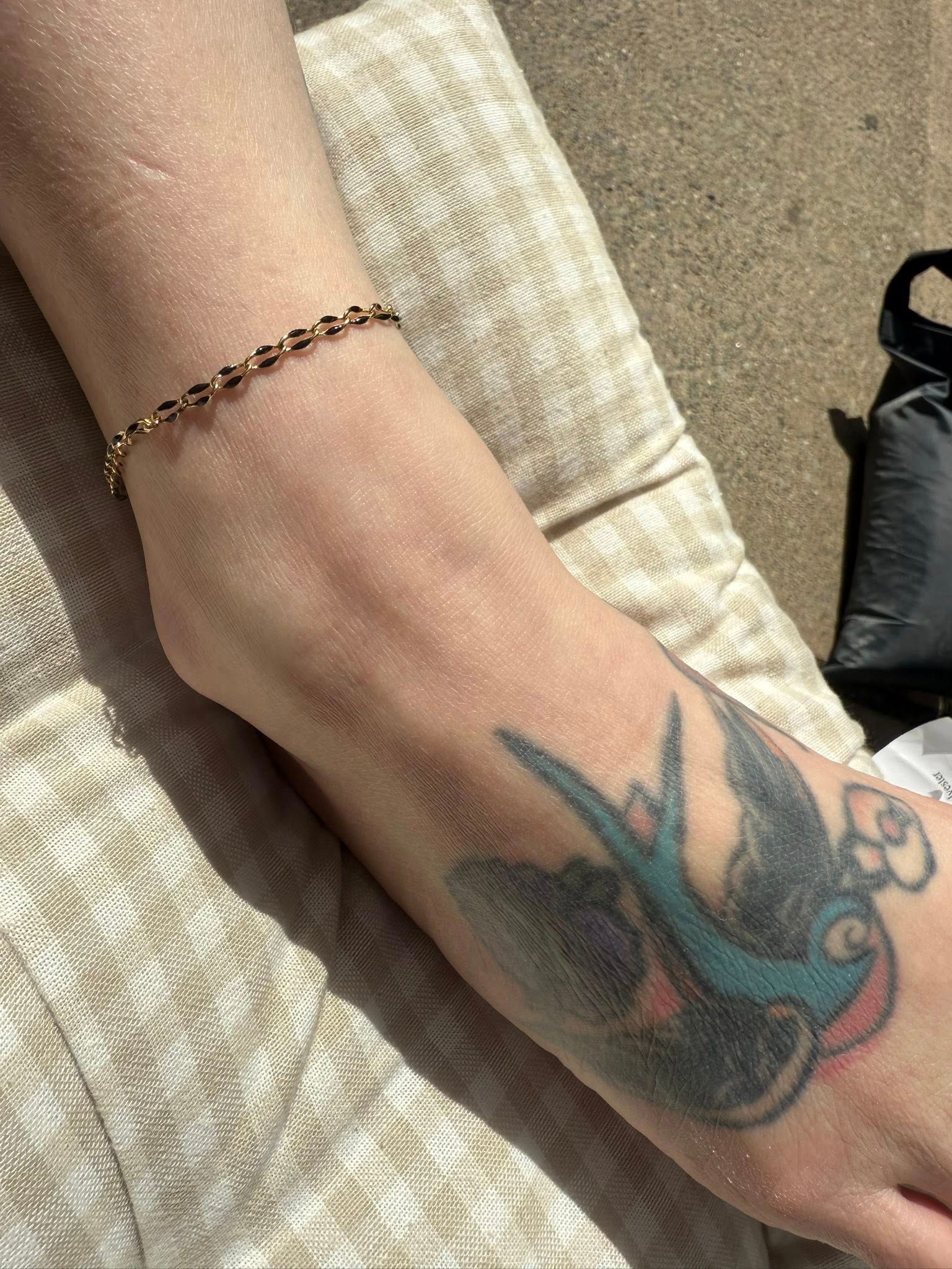 Close-up of a wrist with a beaded bracelet and a colorful bird tattoo on the hand, resting on a woven chair.