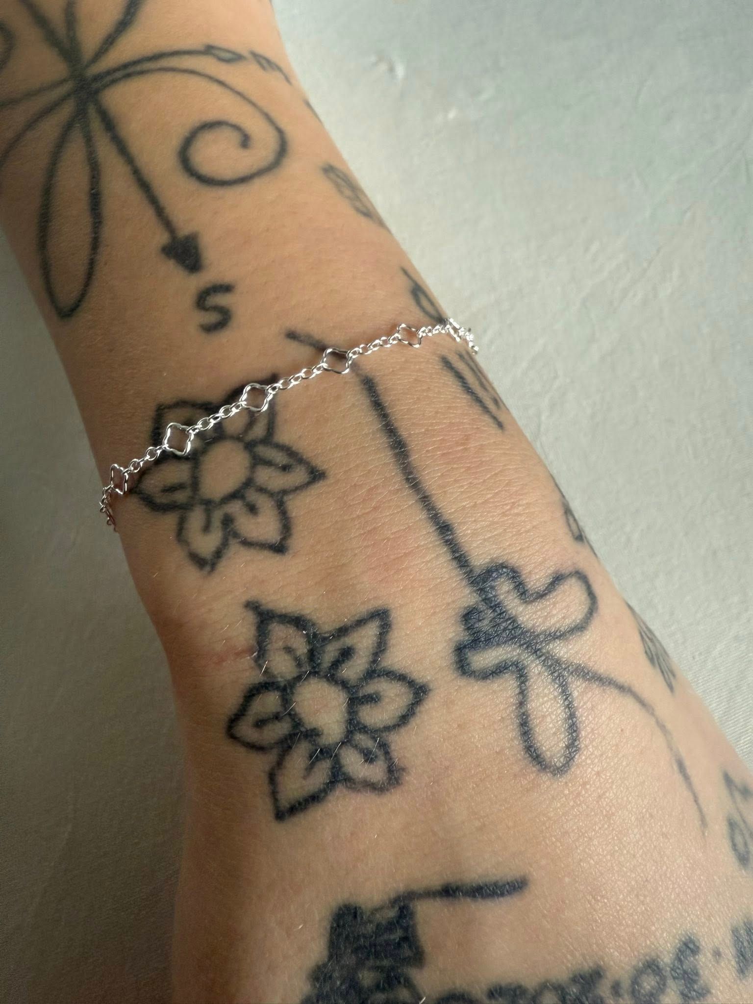 Arm with floral vine tattoos and a silver bracelet on a light background