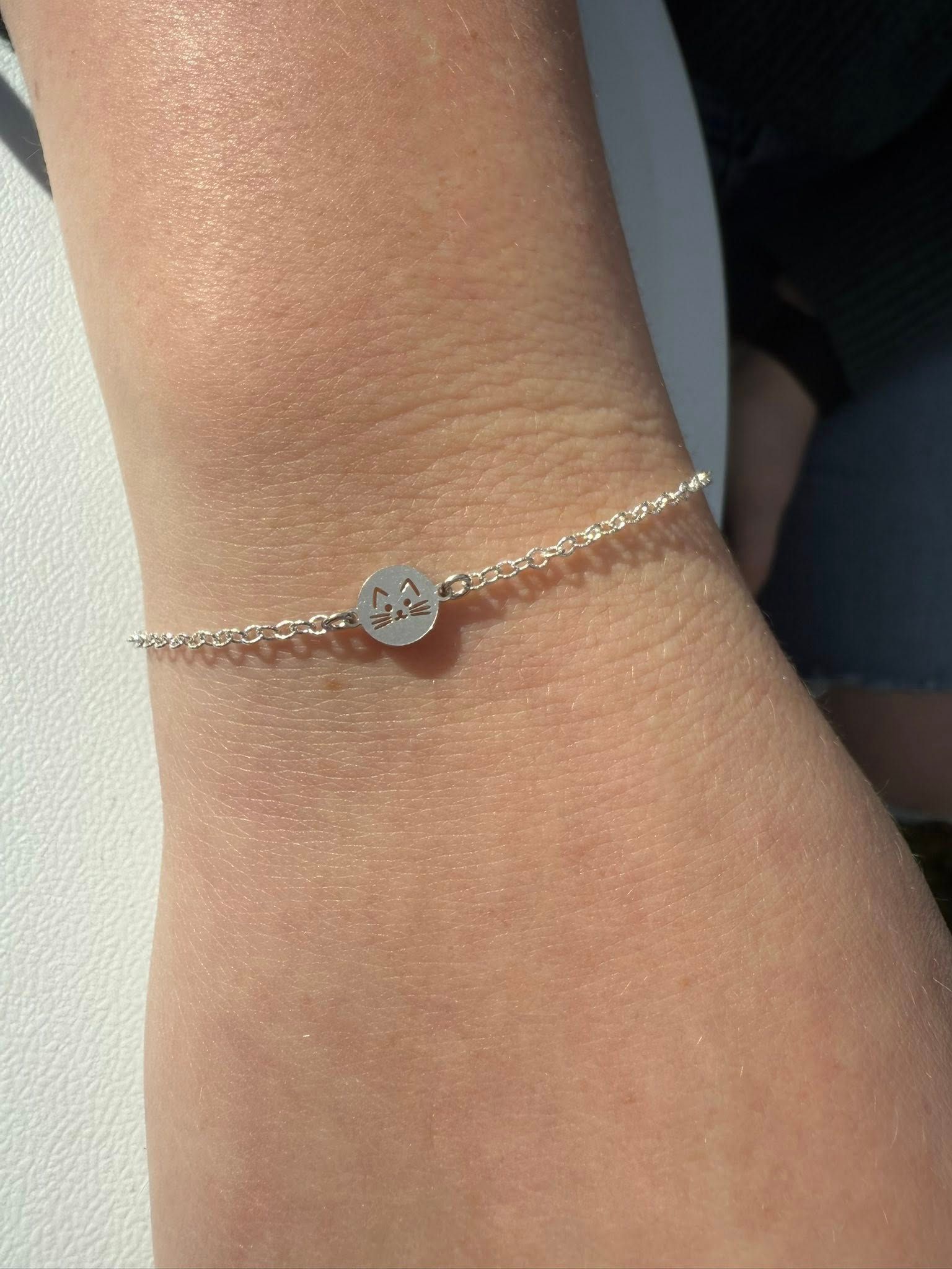 Close-up of a wrist wearing a delicate silver bracelet with a small round charm