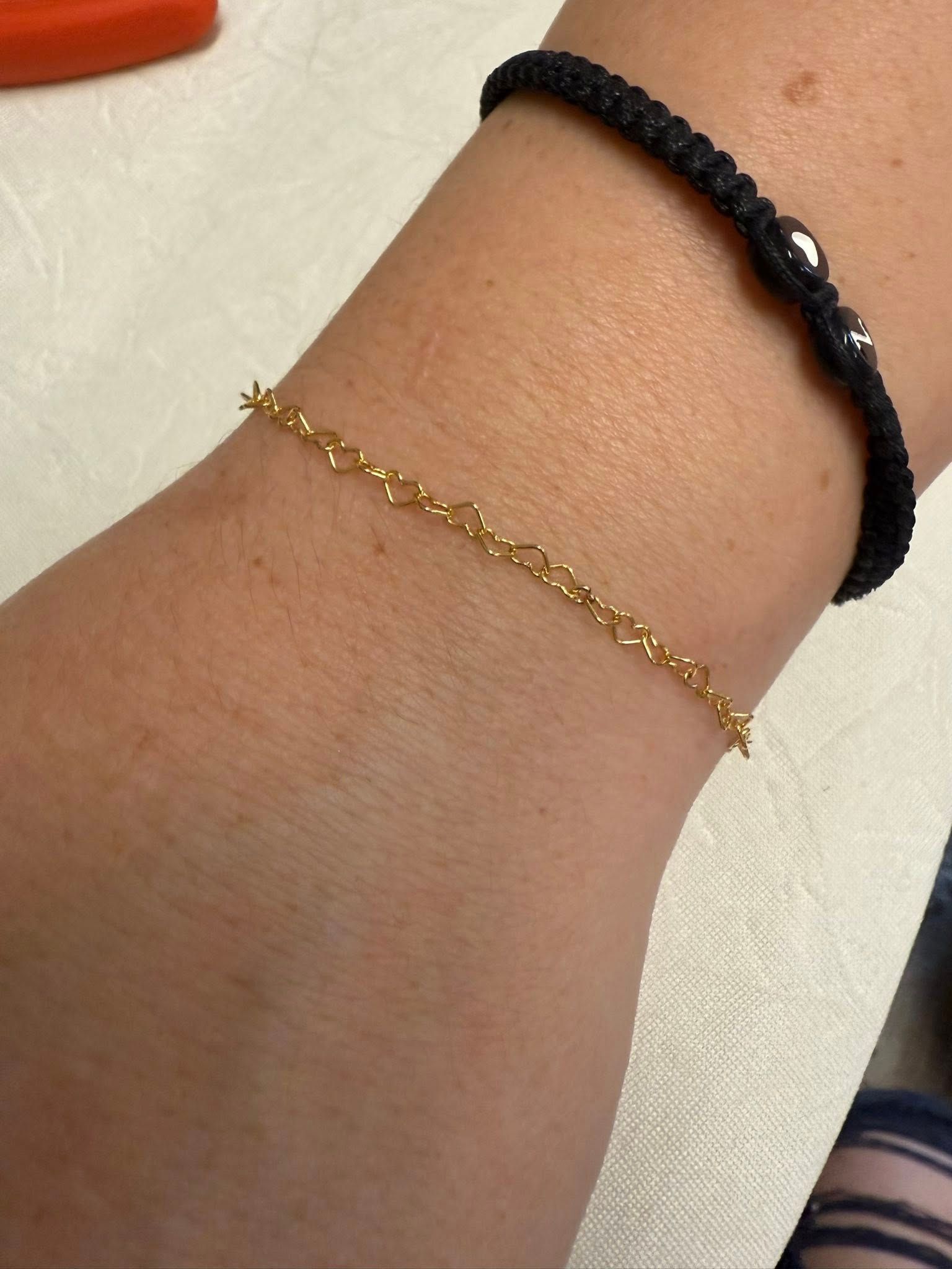 Two bracelets on a wrist: a black braided band and a thin gold chain.