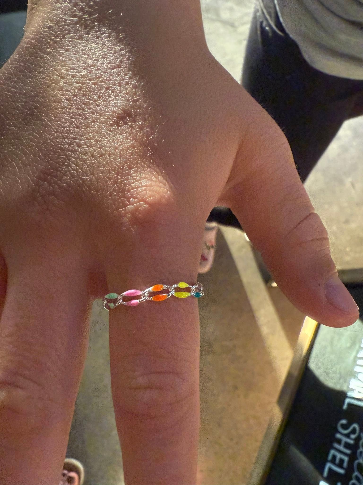 Close-up of a hand wearing a colorful beaded ring on the middle finger.
