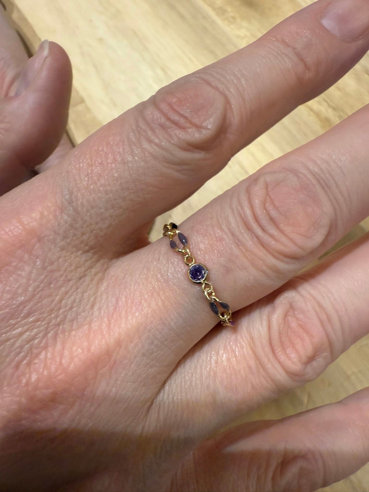 Close-up of a hand wearing a delicate gold ring with small purple gemstones on a wooden surface