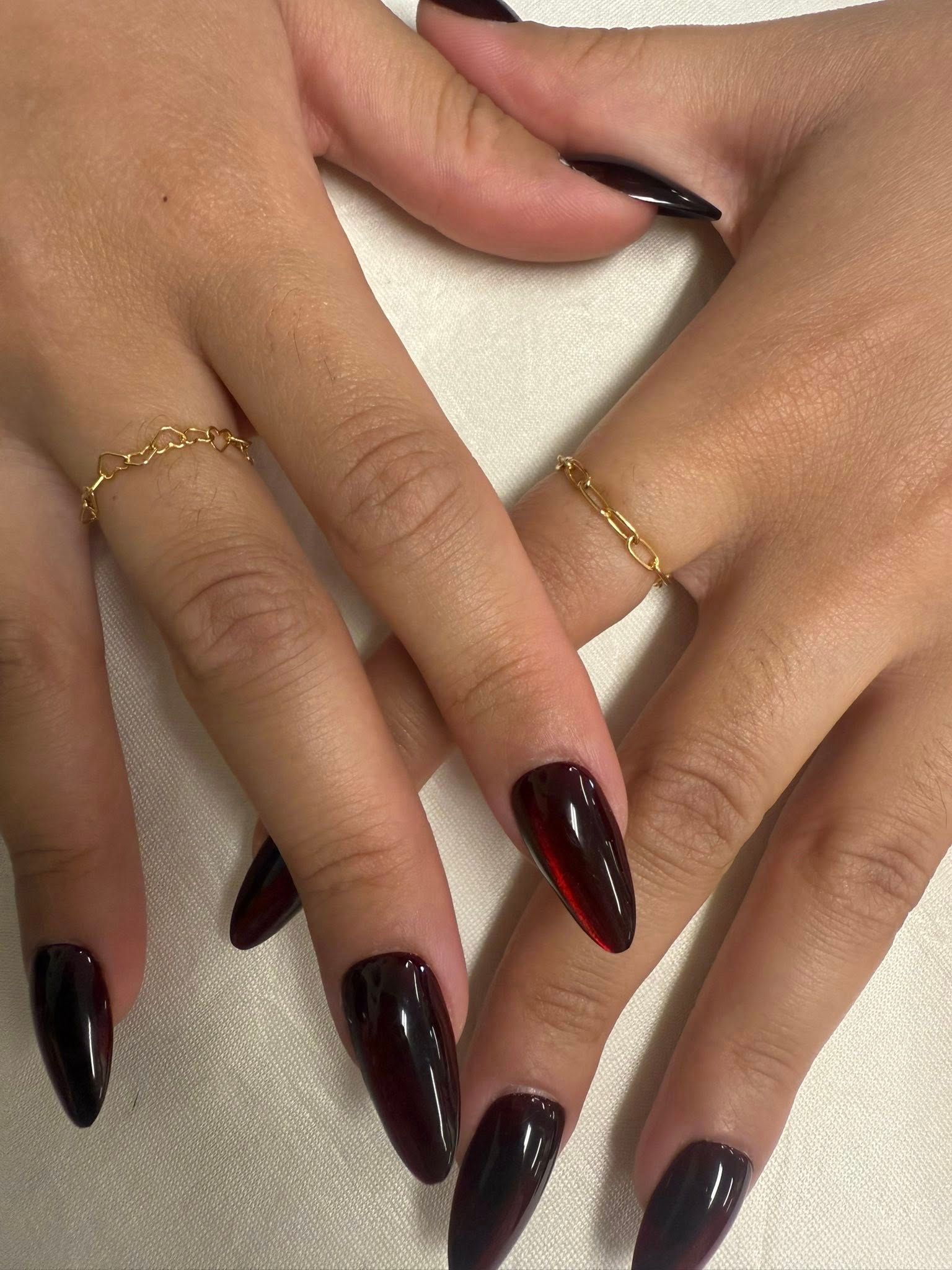 Hands with long burgundy nails and delicate gold rings on a white textured background
