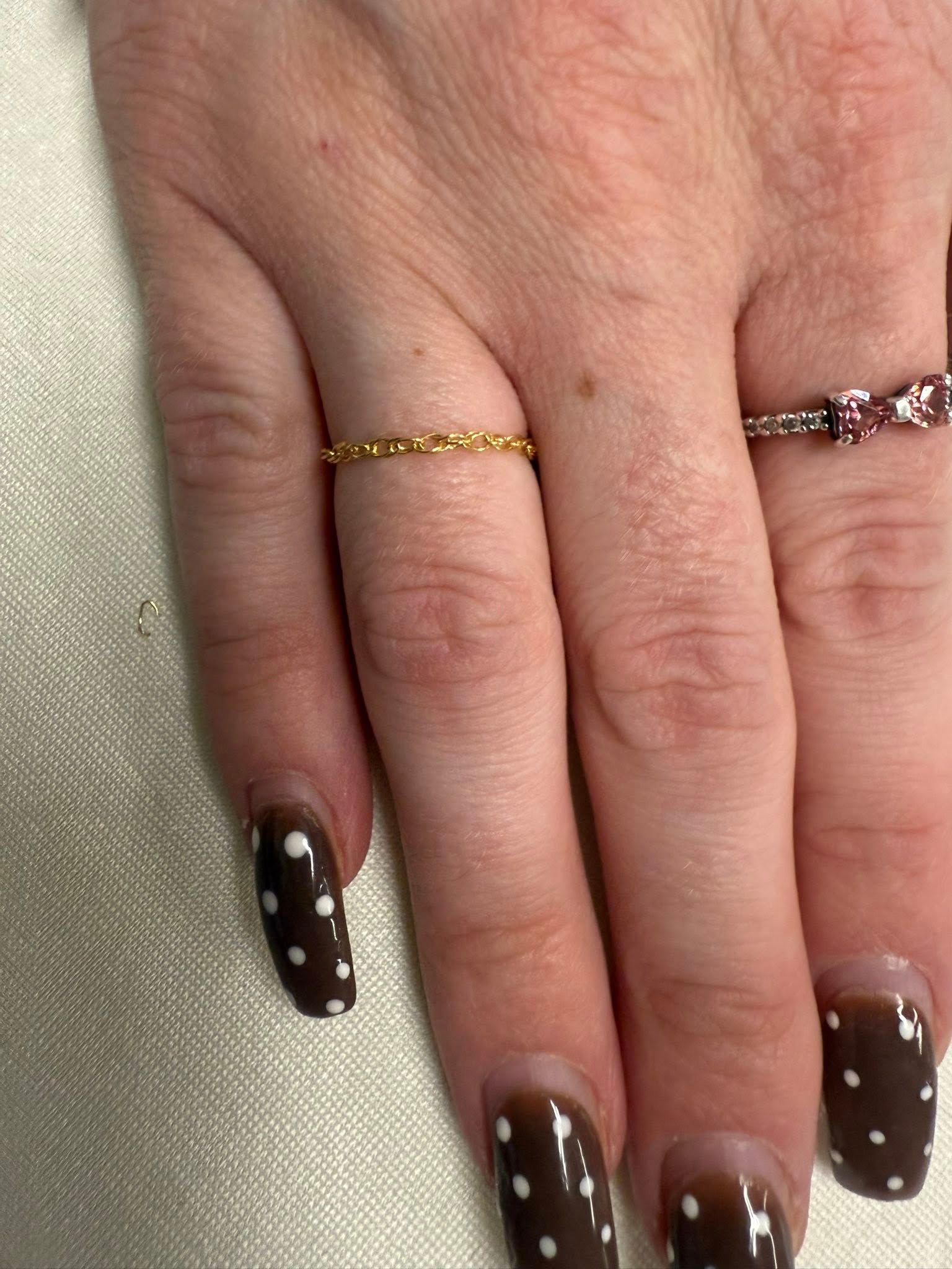 Hand with brown polka-dot nails and two rings on a light fabric background