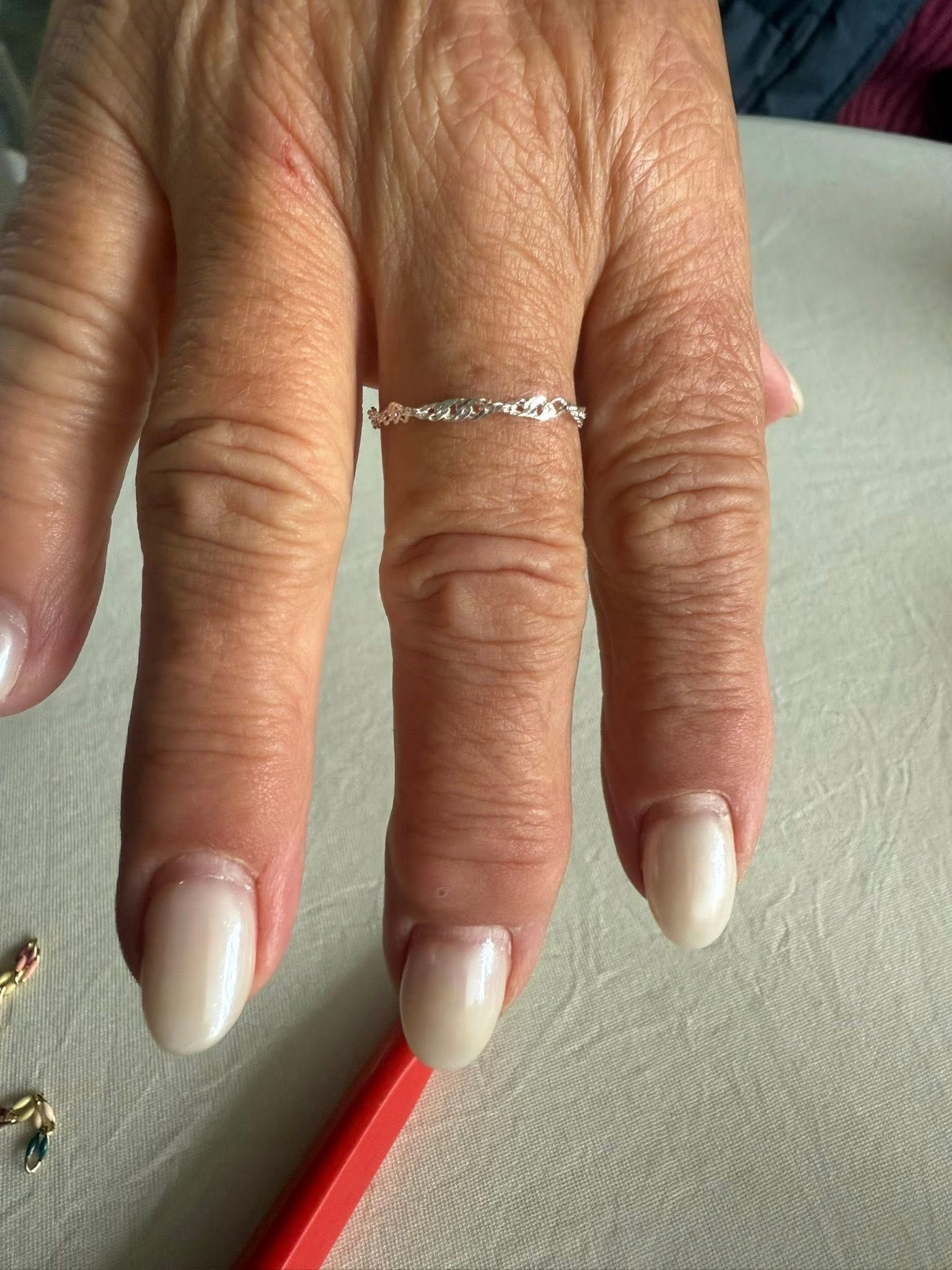 Hand with white manicured nails and a thin silver ring resting on a light fabric surface.