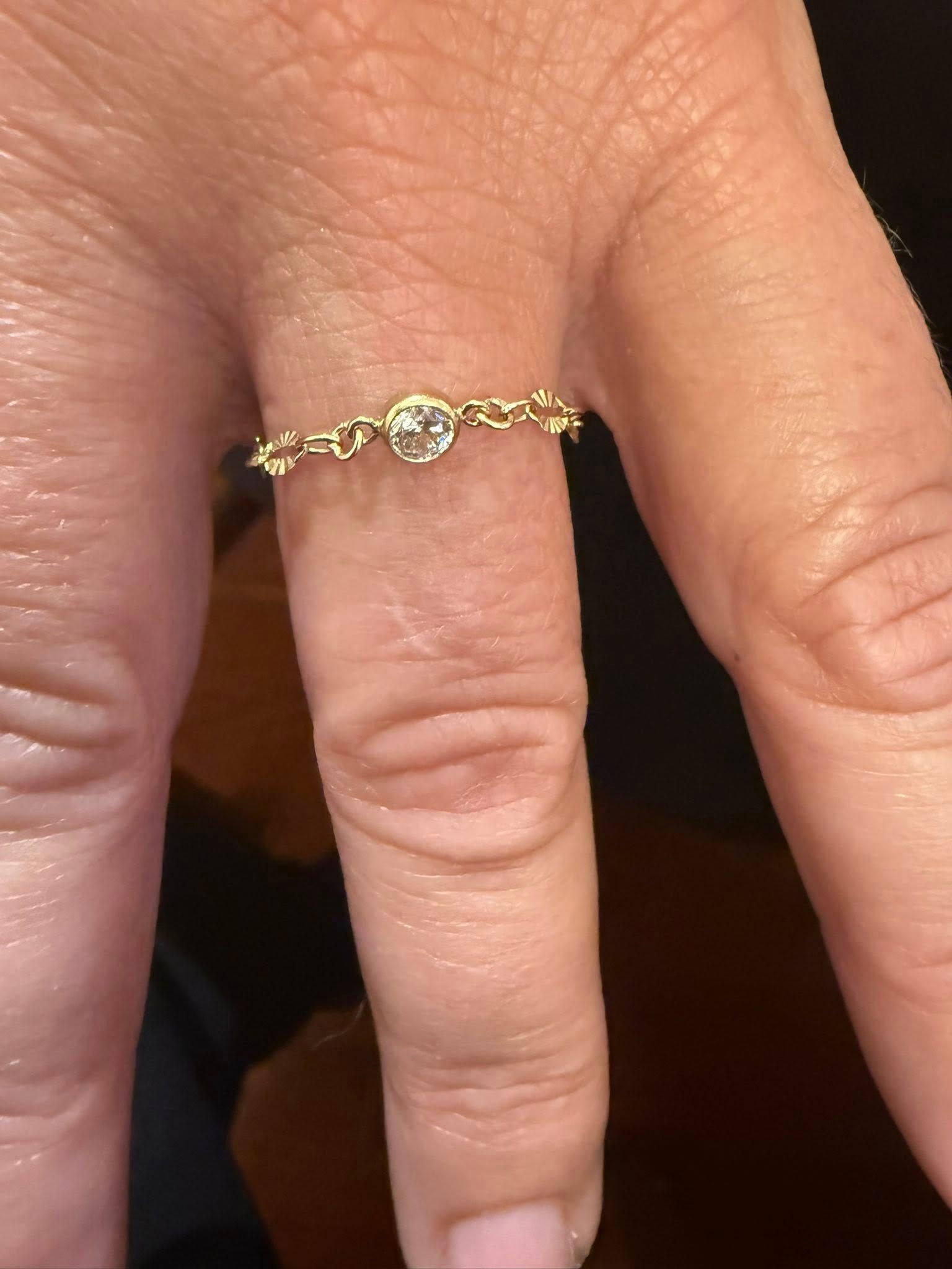Close-up of a hand wearing a thin gold ring with small heart details on the finger.