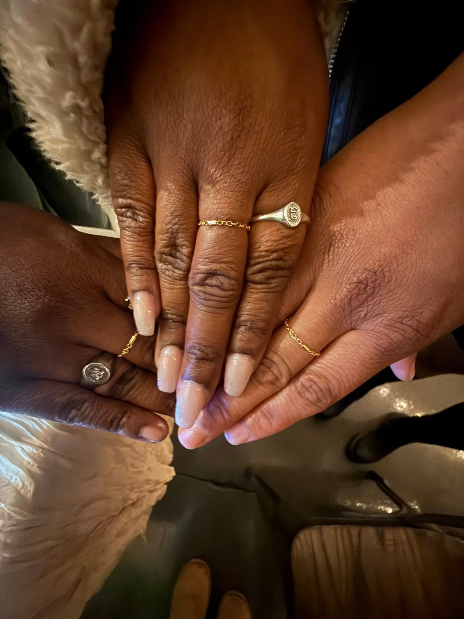 Hands with manicured nails and rings stacked together in a circle, viewed from above.