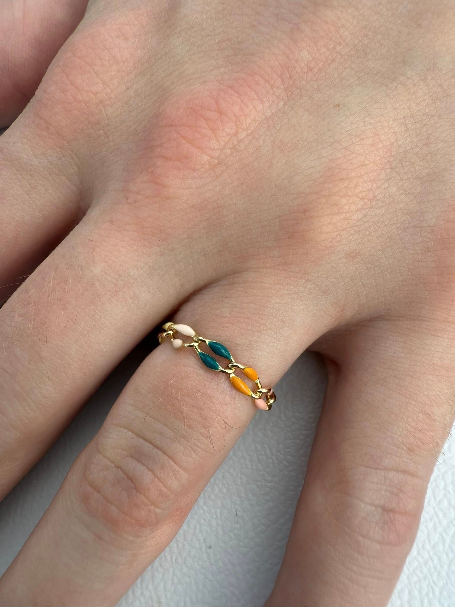 Hand wearing a gold ring with green and amber stones on a gray surface