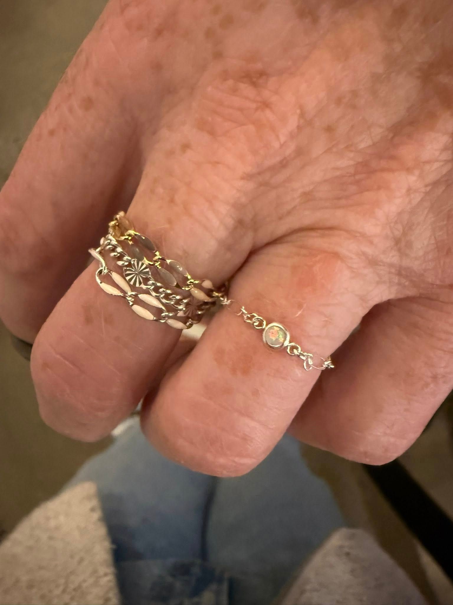 Close-up of a hand wearing delicate gold rings with a linked chain design.
