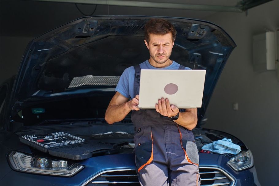 Mechanic holding a laptop in front of an open car hood in a garage