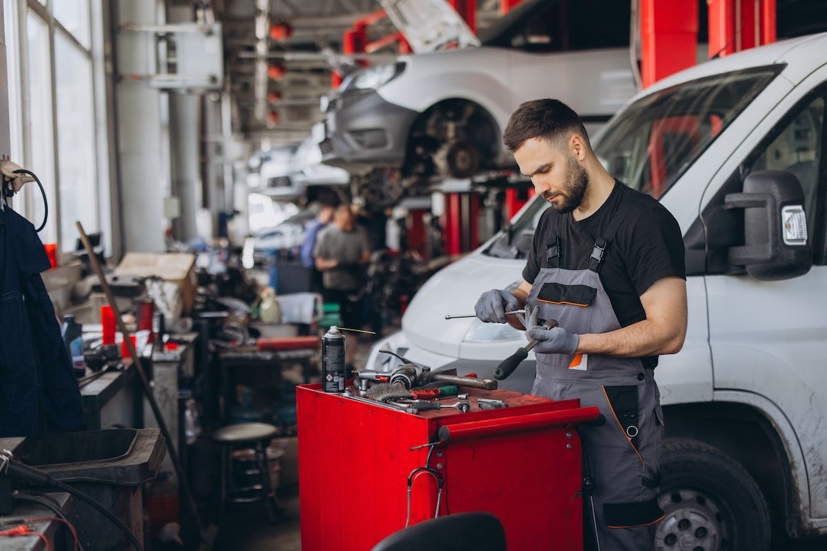 Mechanic working beside a red tool cart in an auto repair shop with lifted cars in the background