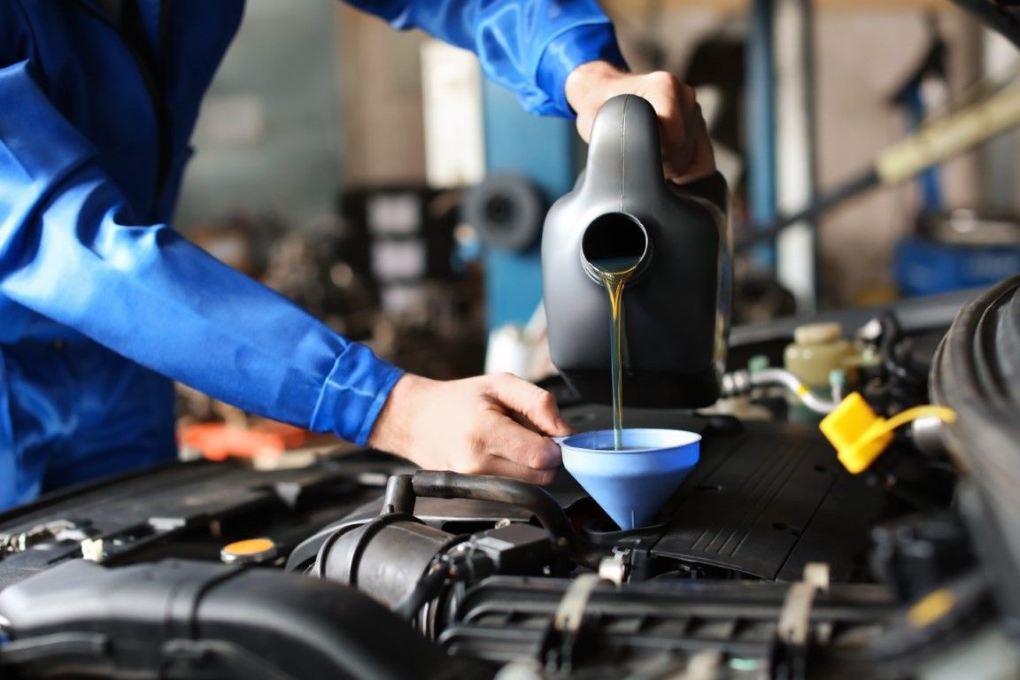 Mechanic pouring engine oil into a car engine using a funnel in a repair shop