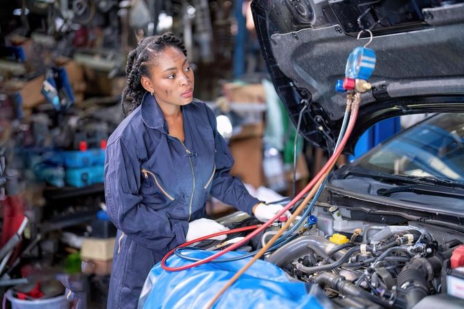 Mechanic using a diagnostic tool on a blue car with the hood open in an auto repair shop