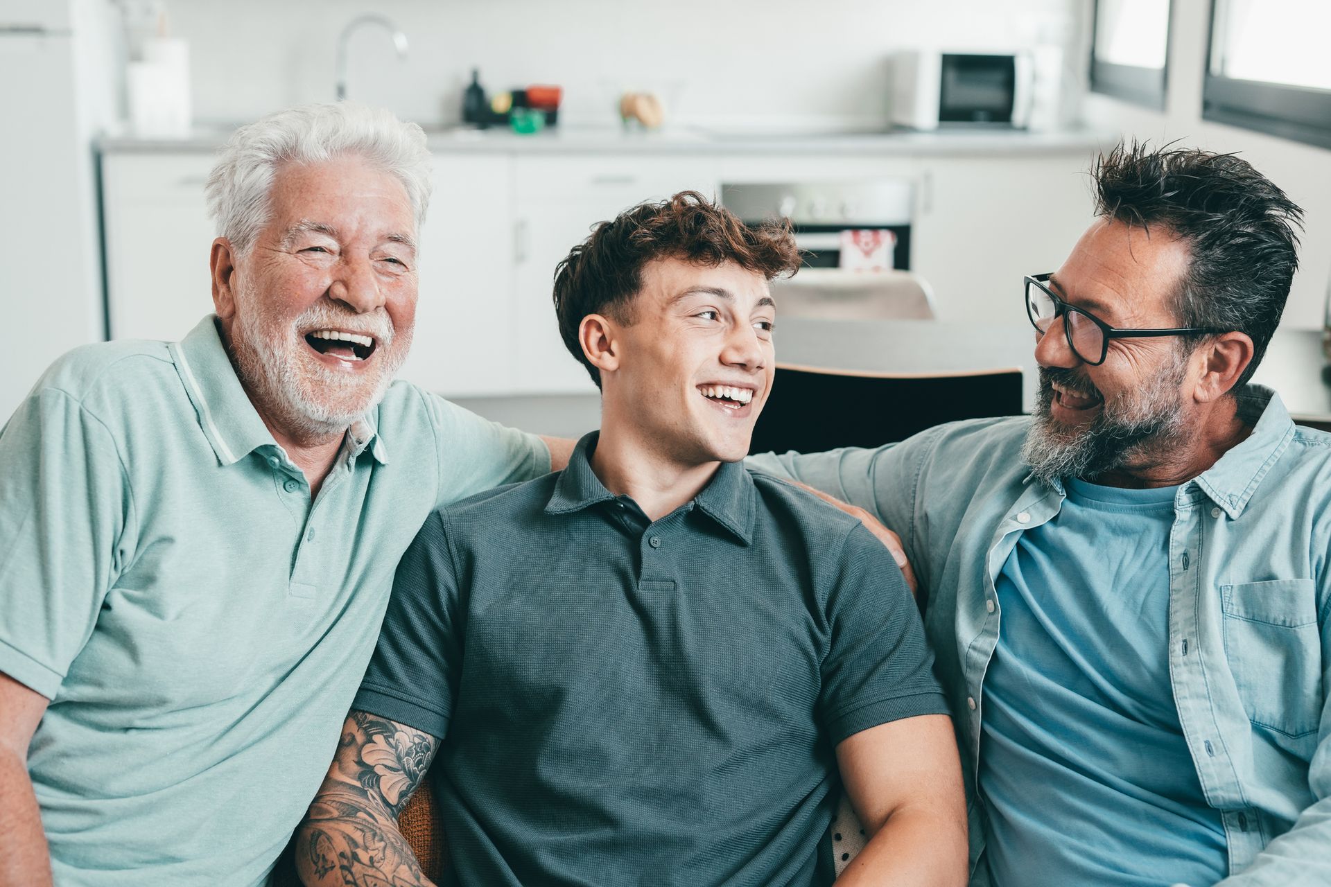 Three men are sitting next to each other on a couch and laughing.