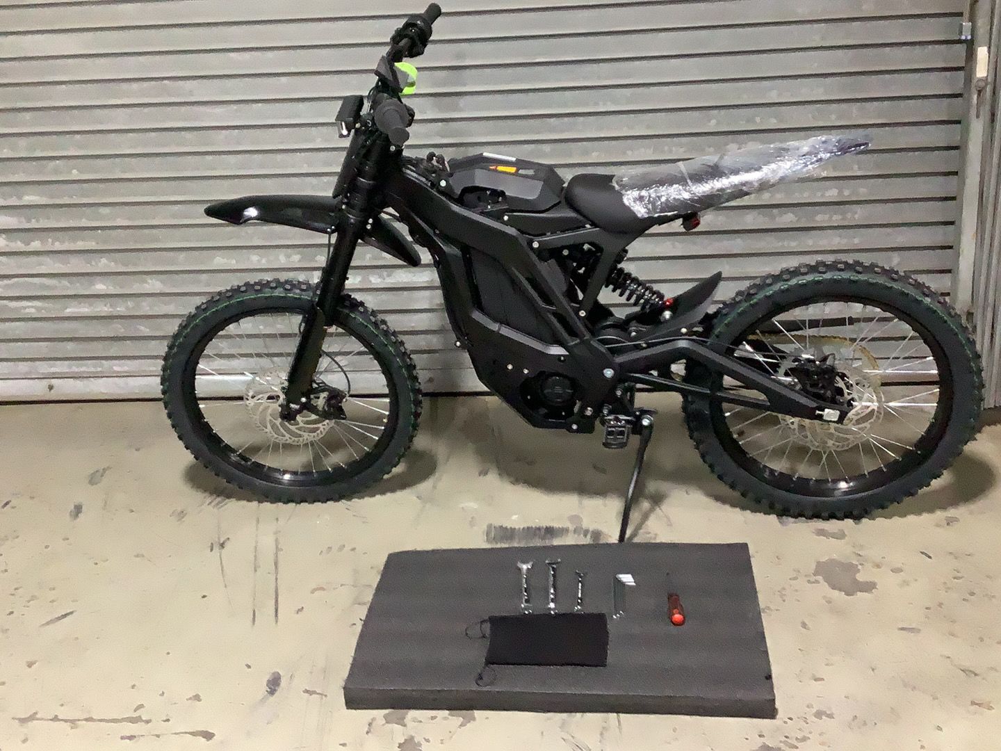 An electric dirt bike is sitting on a mat in front of a garage door.