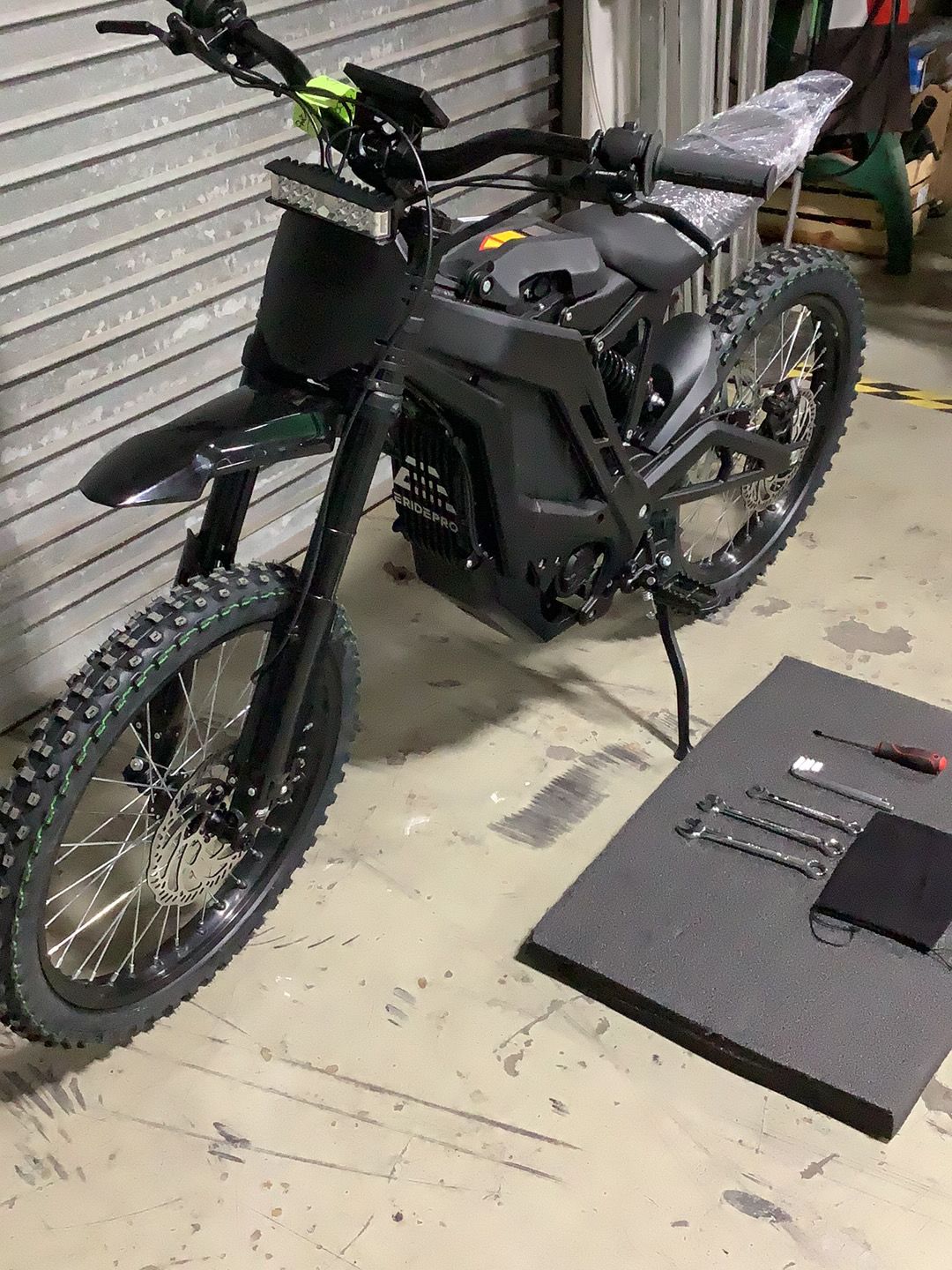 An electric dirt bike is sitting on the floor in a garage.