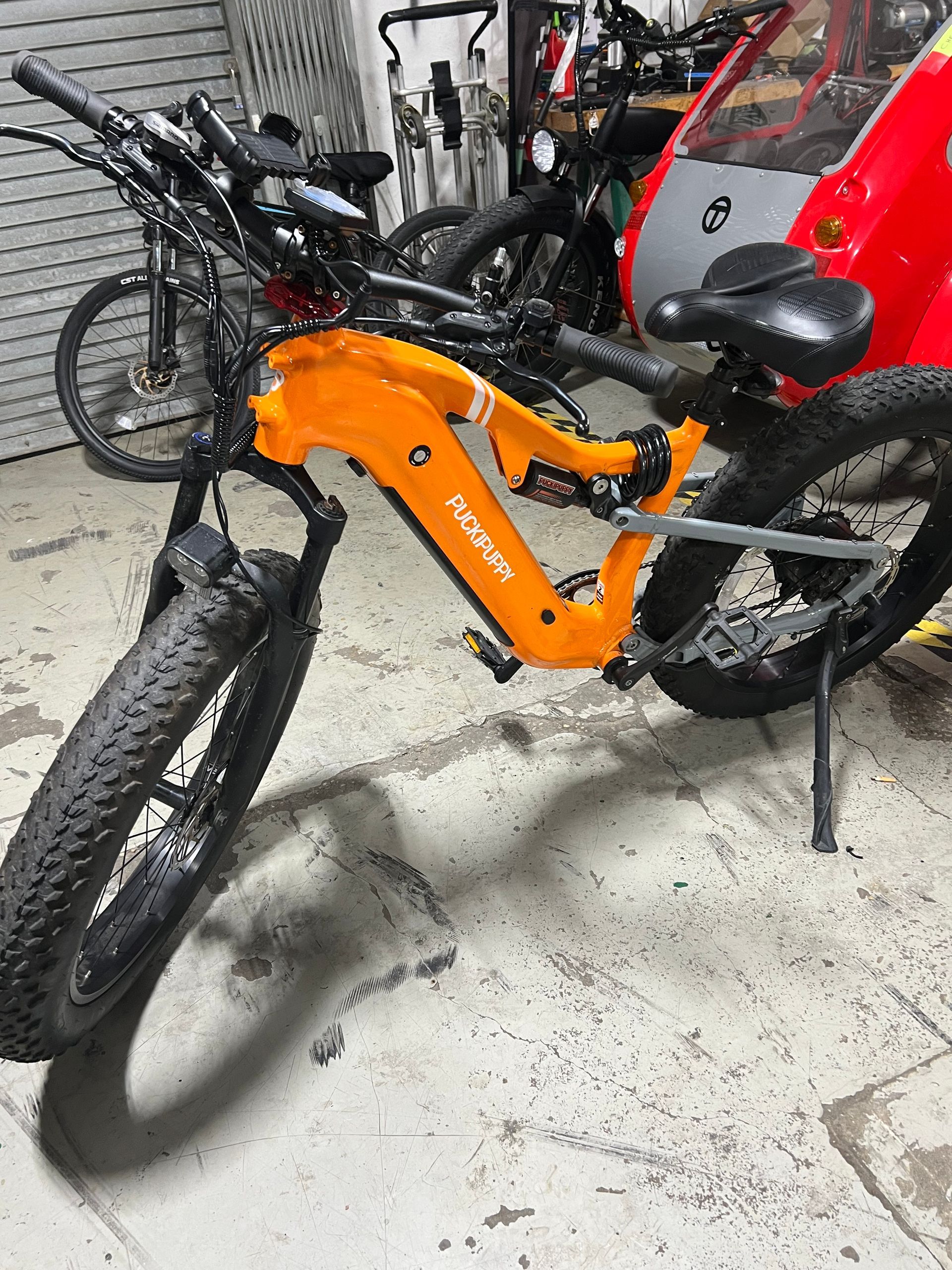 An orange electric bike is parked in a garage next to other bikes.