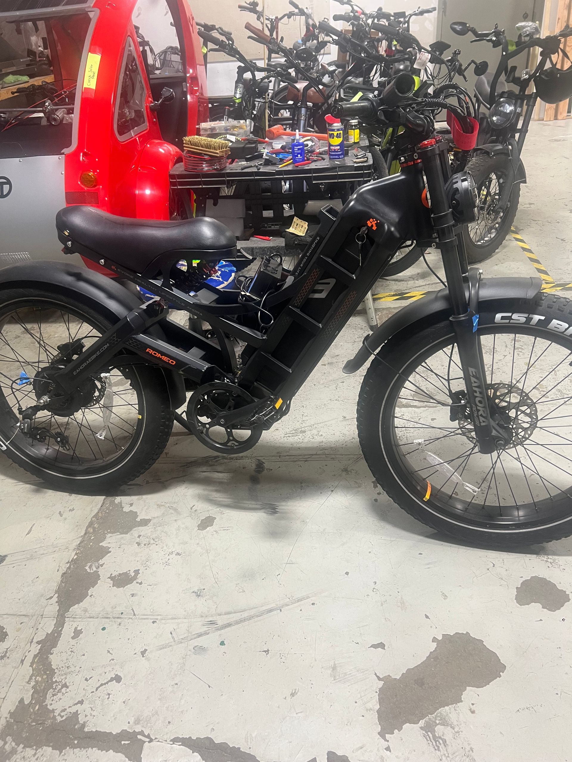 A black electric bike is parked in a garage next to a red car.