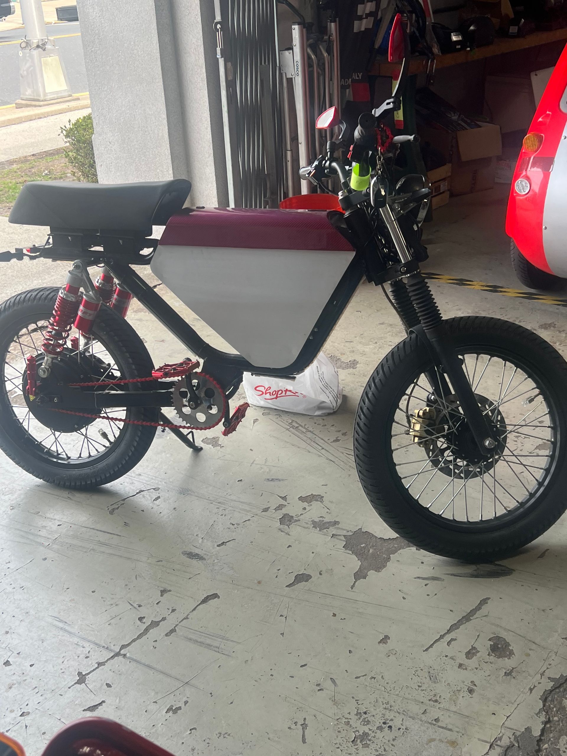 A motorcycle is parked in a garage next to a red and white car.