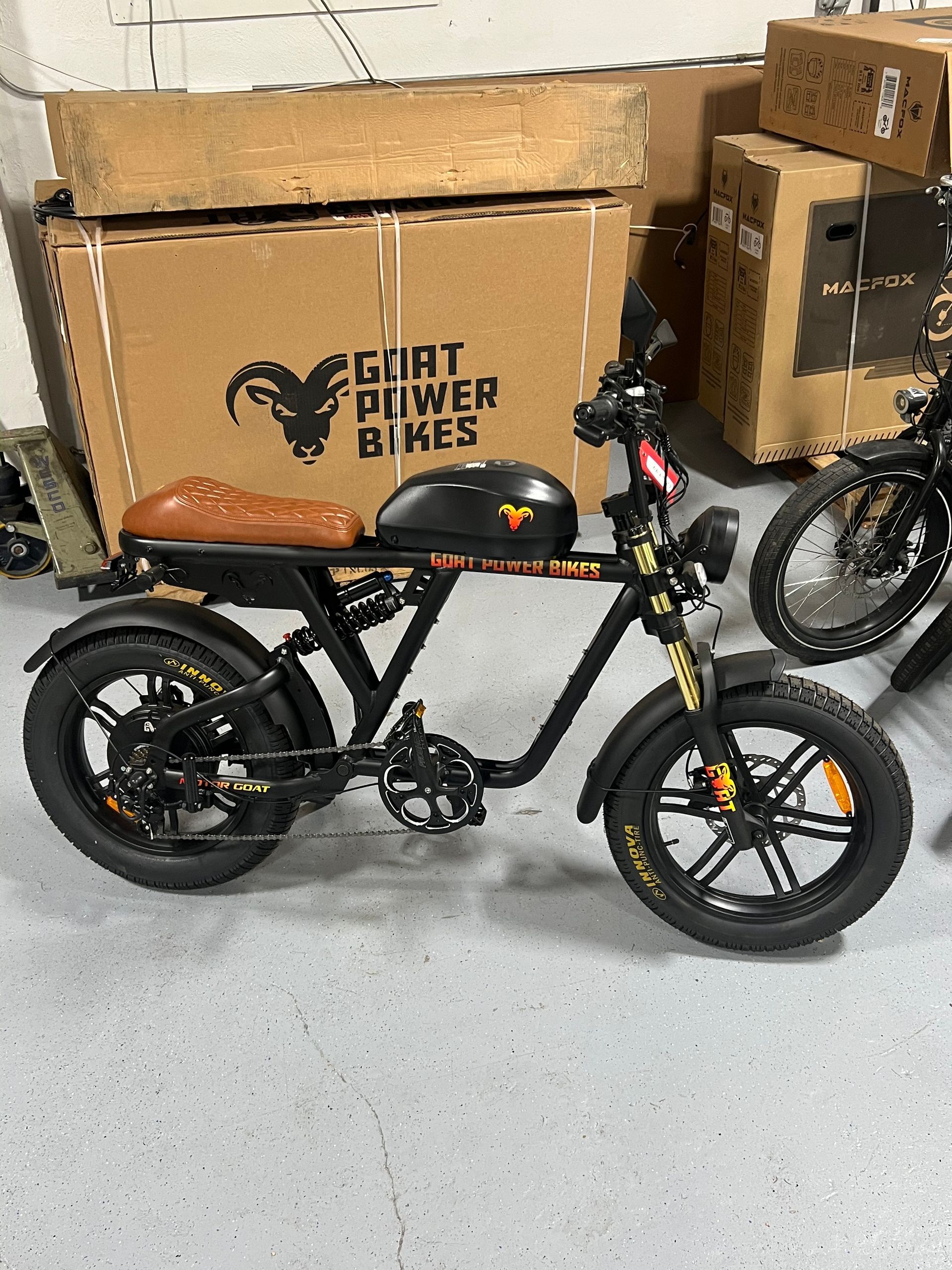 A motorcycle is parked in front of a cardboard box that says goat power bikes.