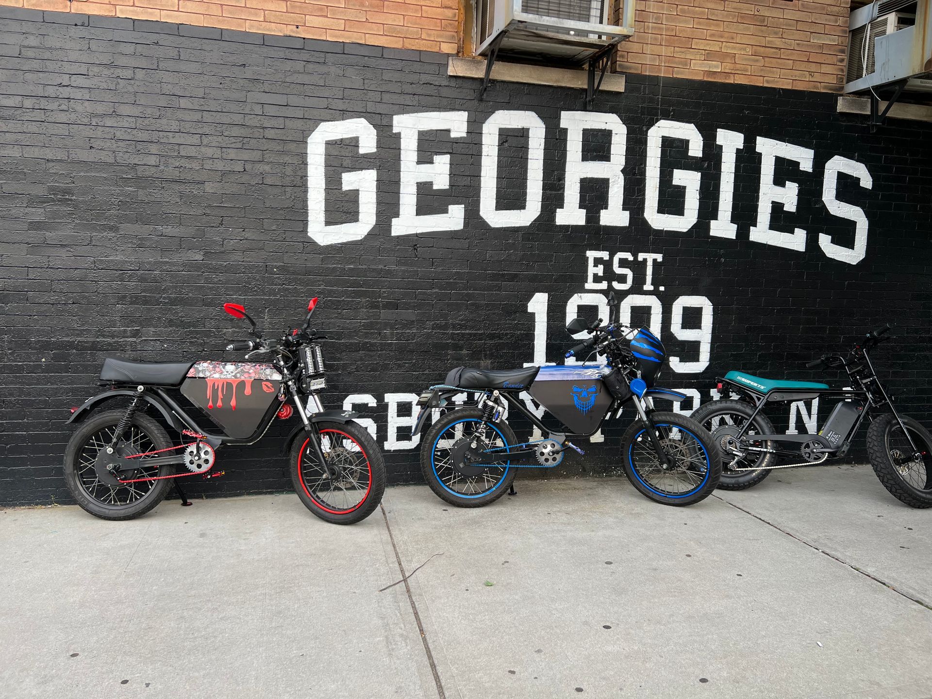 Three motorcycles are parked in front of a wall that says georgies