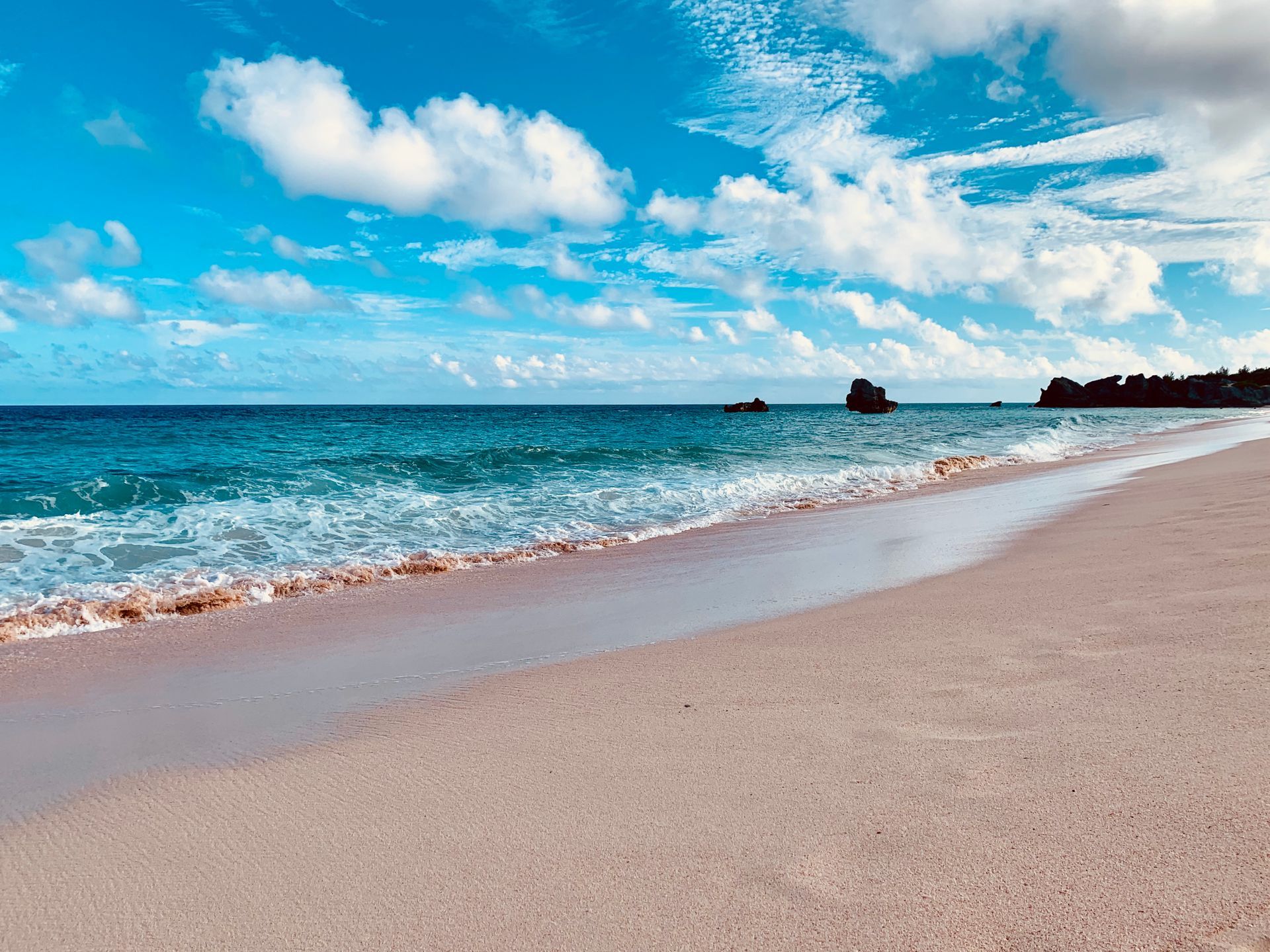 Sunny beach with turquoise waves, white clouds, and a sandy shoreline.