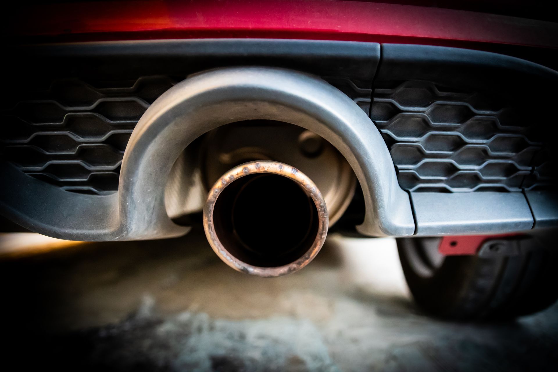 Exhaust pipe of a red car, showing a close-up view of the tailpipe and surrounding bumper detail.