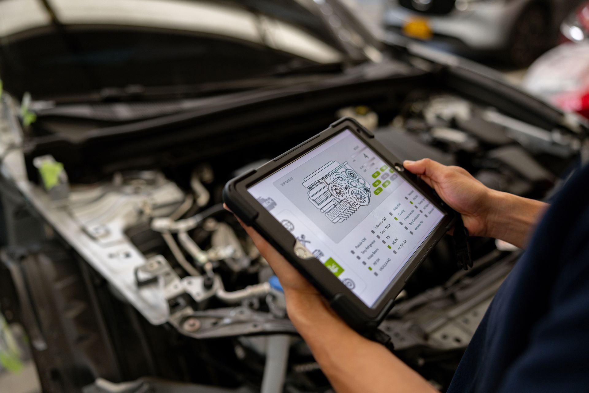 Mechanic using tablet to diagnose car engine. White vehicle and tools visible in shop.