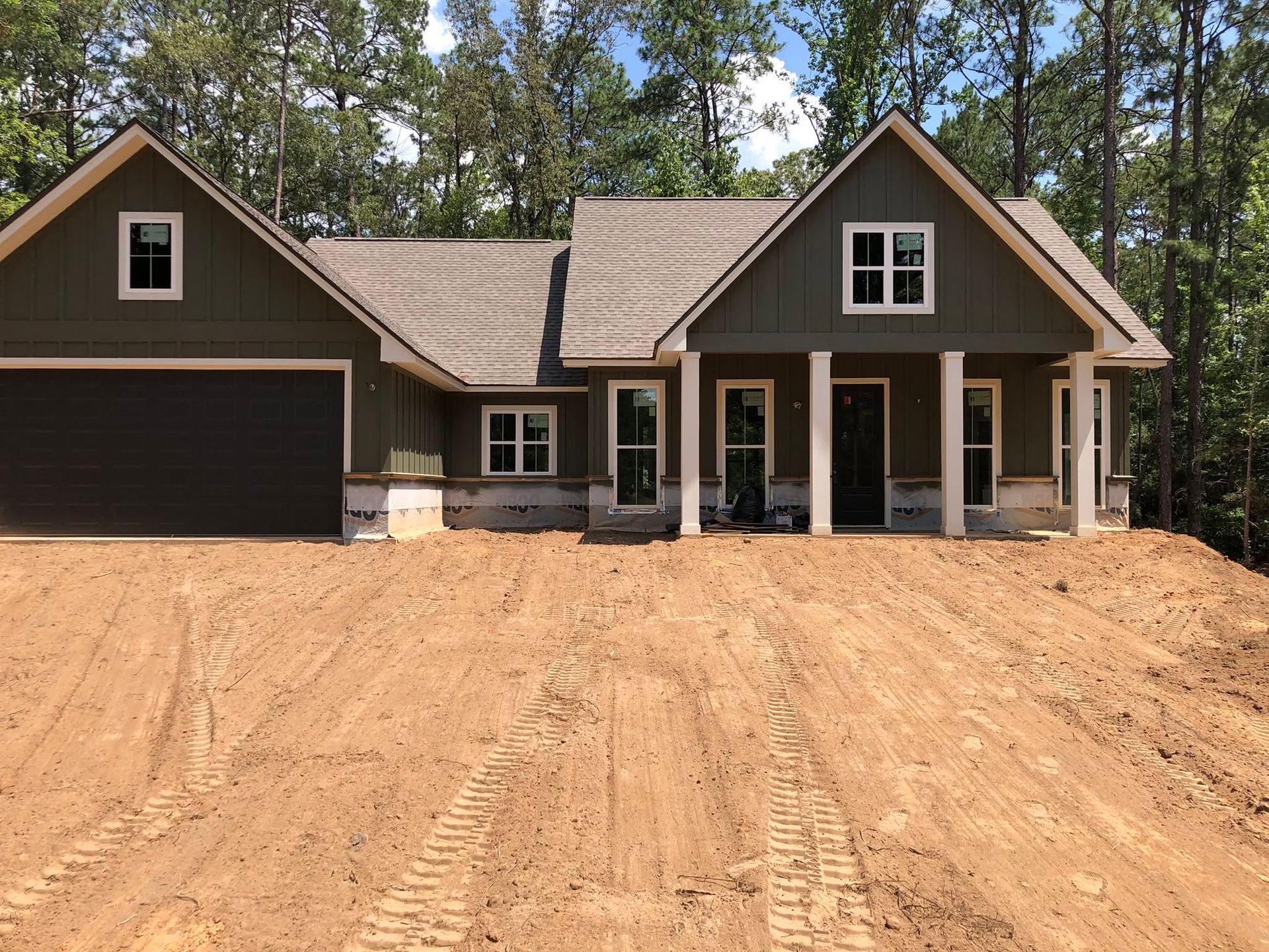 New dark-trim house with garage, front porch, and bare dirt yard under construction