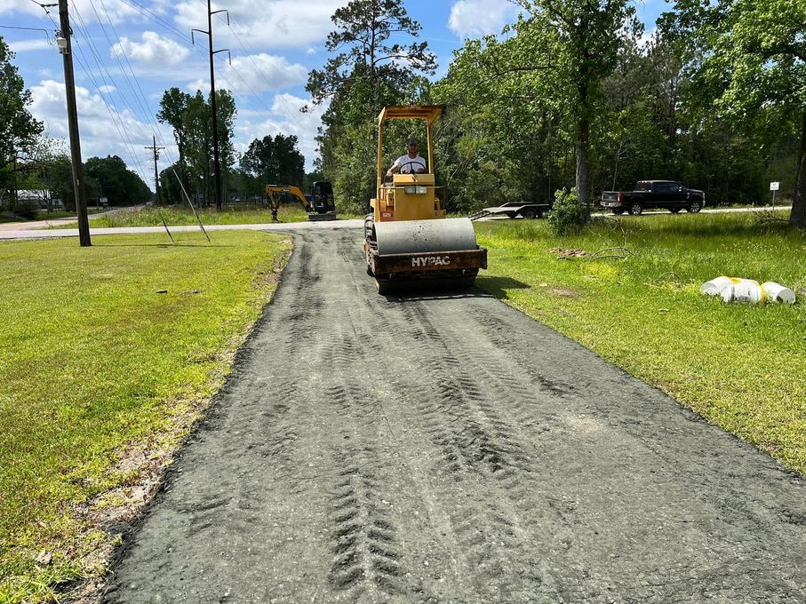 Road roller compacting a gravel path in a grassy park under a blue sky.