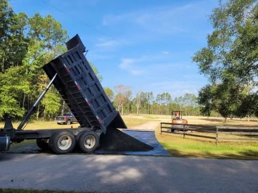 Dump truck bed raised, unloading a pile of dirt on a rural roadside.