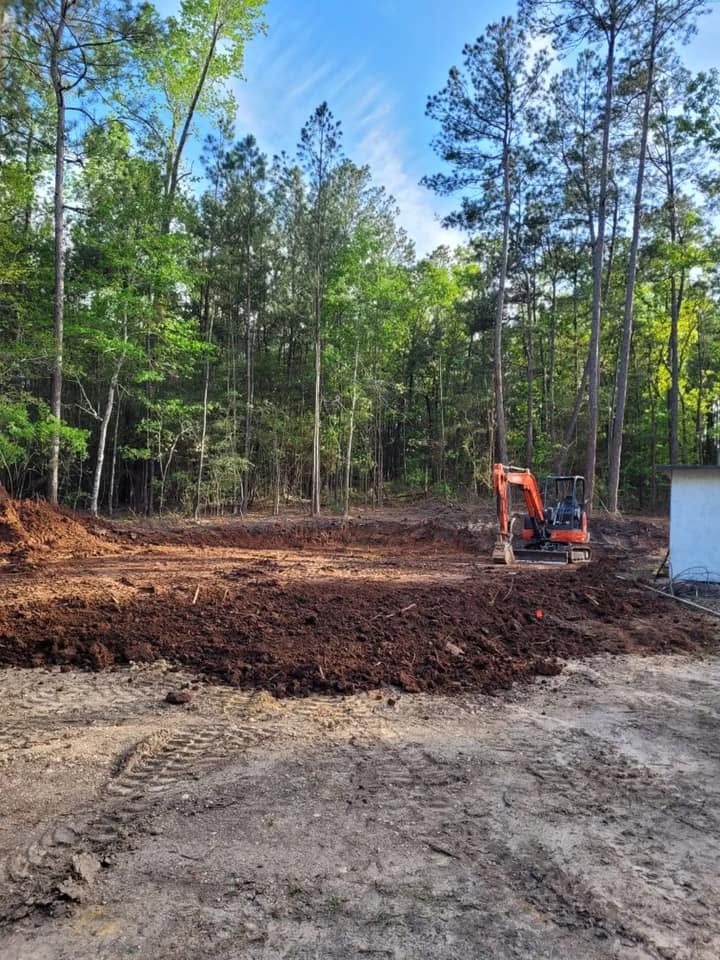 Orange excavator clearing dirt in a wooded construction site beside a white structure.