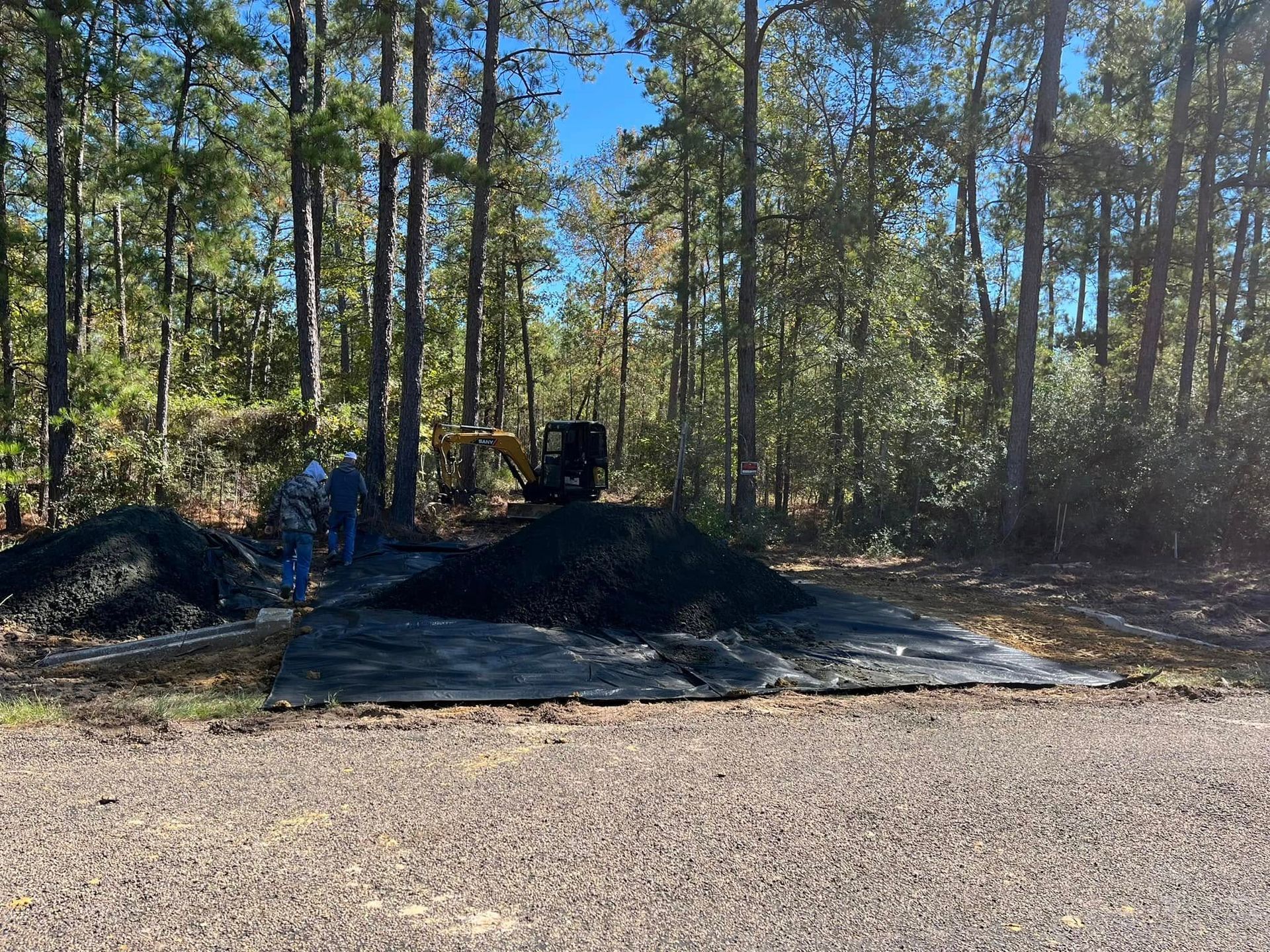 Wooded lot with large black mulch piles and black tarps spread on the ground