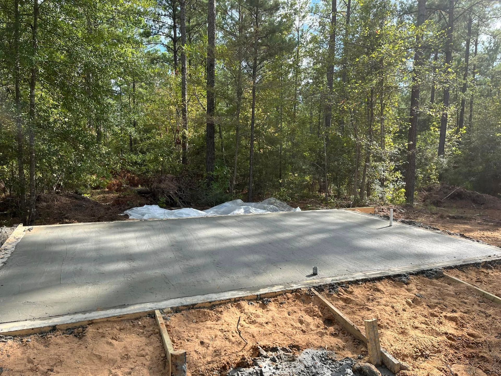 Fresh concrete slab in a wooded area, with snow along the back edge and dirt in the foreground.