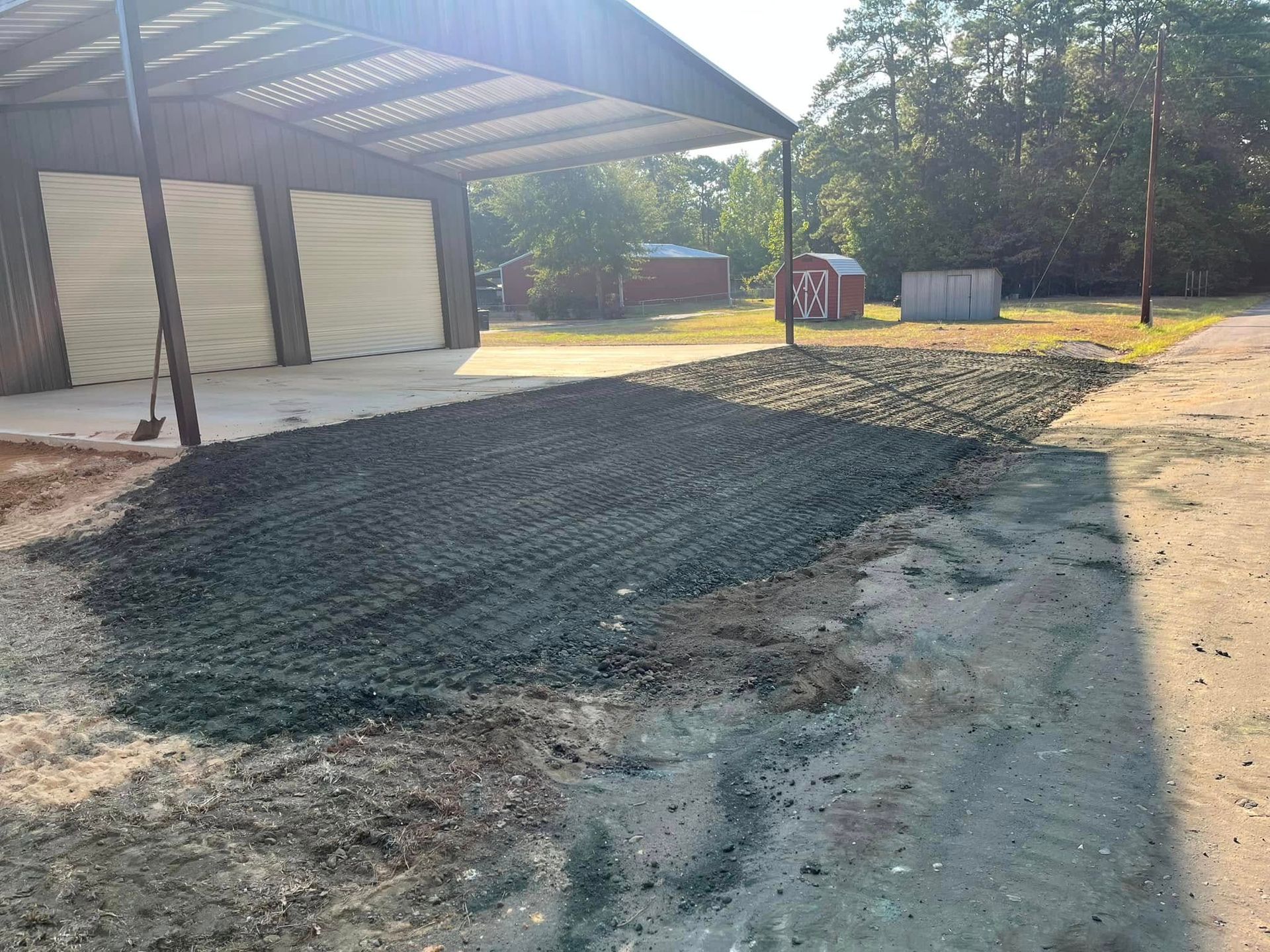 Fresh gravel spread in a driveway beside a carport and garage, with trees and yard in the background