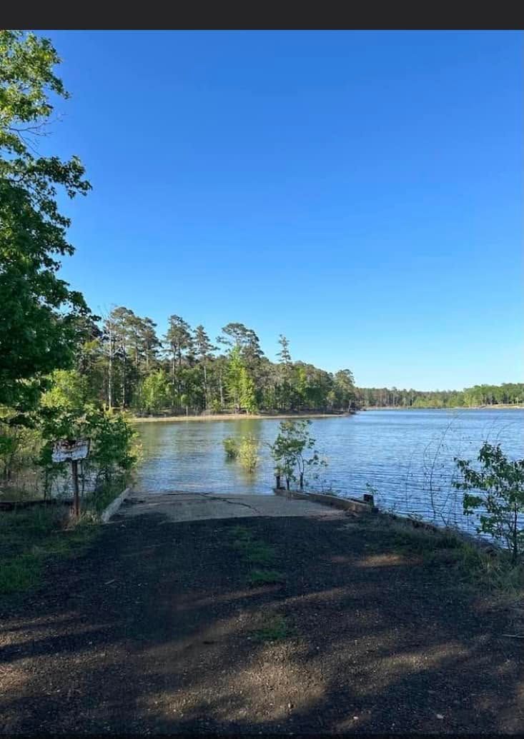 Quiet lakeshore with trees, blue sky, and a small sandy launch area in the foreground