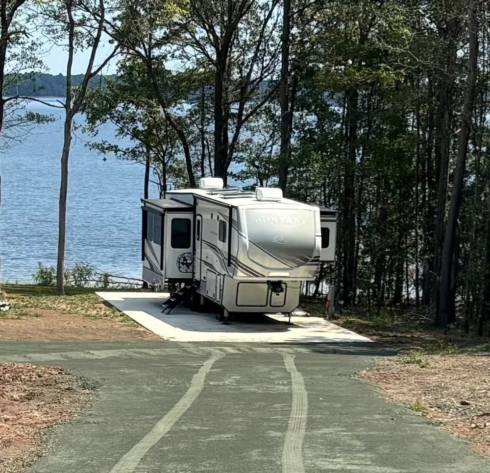 White camper trailer parked at a lakeside campsite among trees and pines