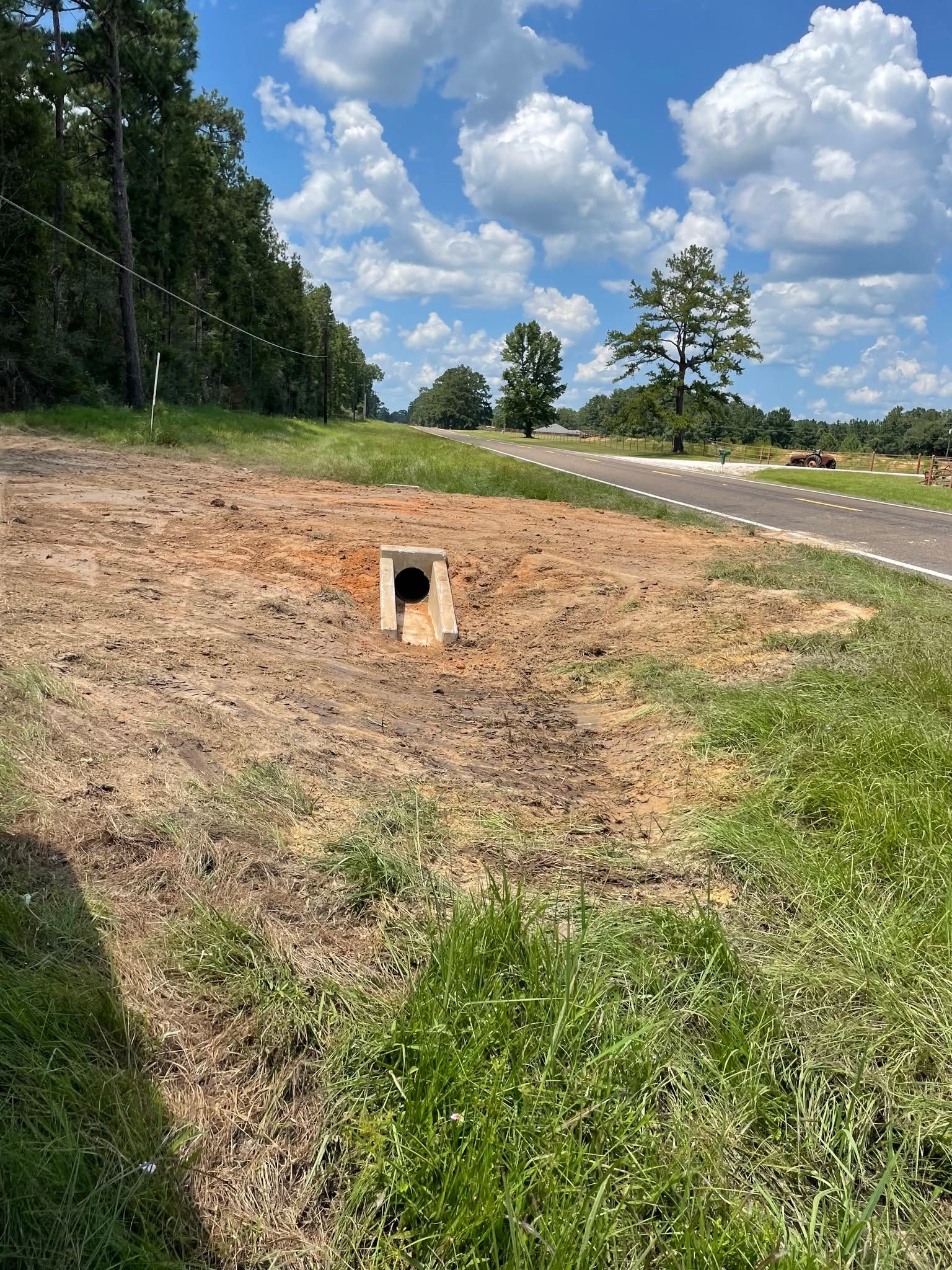 Concrete drainage culvert beside a rural road under a bright blue sky with clouds