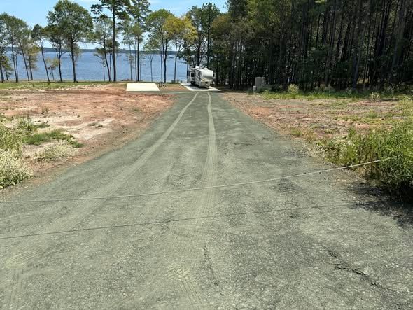 Gravel road leading to a lakeside area with trees and a small dock ahead under clear daylight