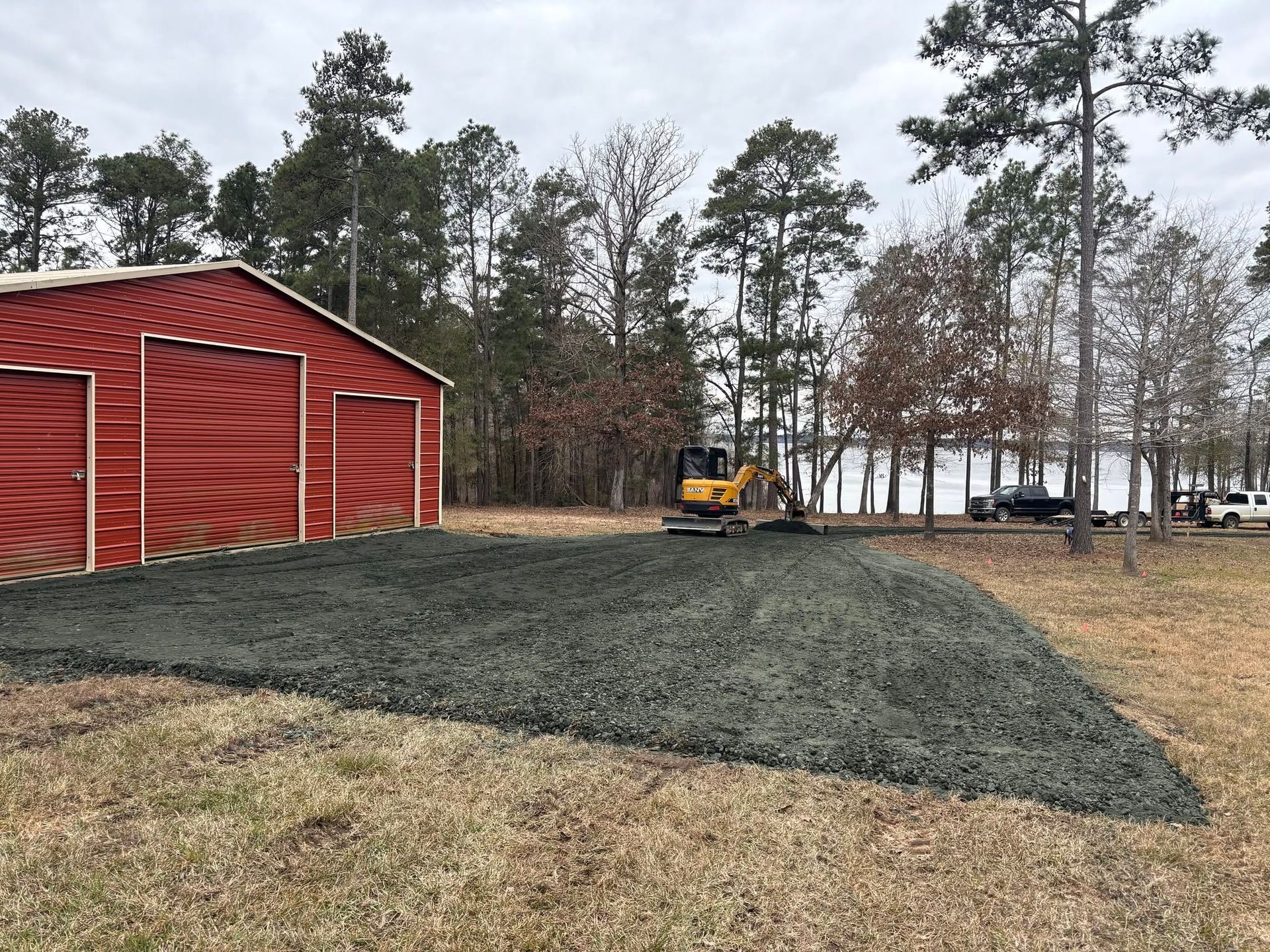 Red barn beside a newly graded gravel lot with a small bulldozer and trees in the background