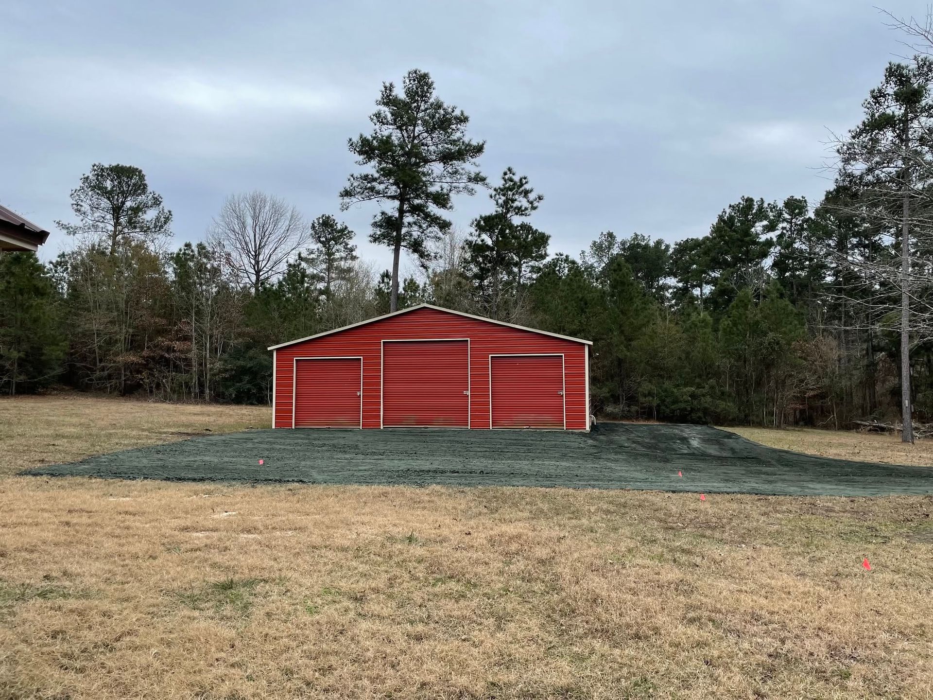 Red barn-style shed on a grassy lot with trees in the background under an overcast sky