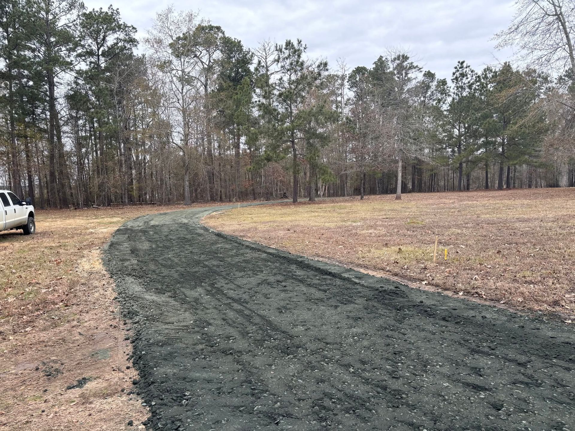 Freshly laid dark gravel path curving through a grassy field with trees in the background