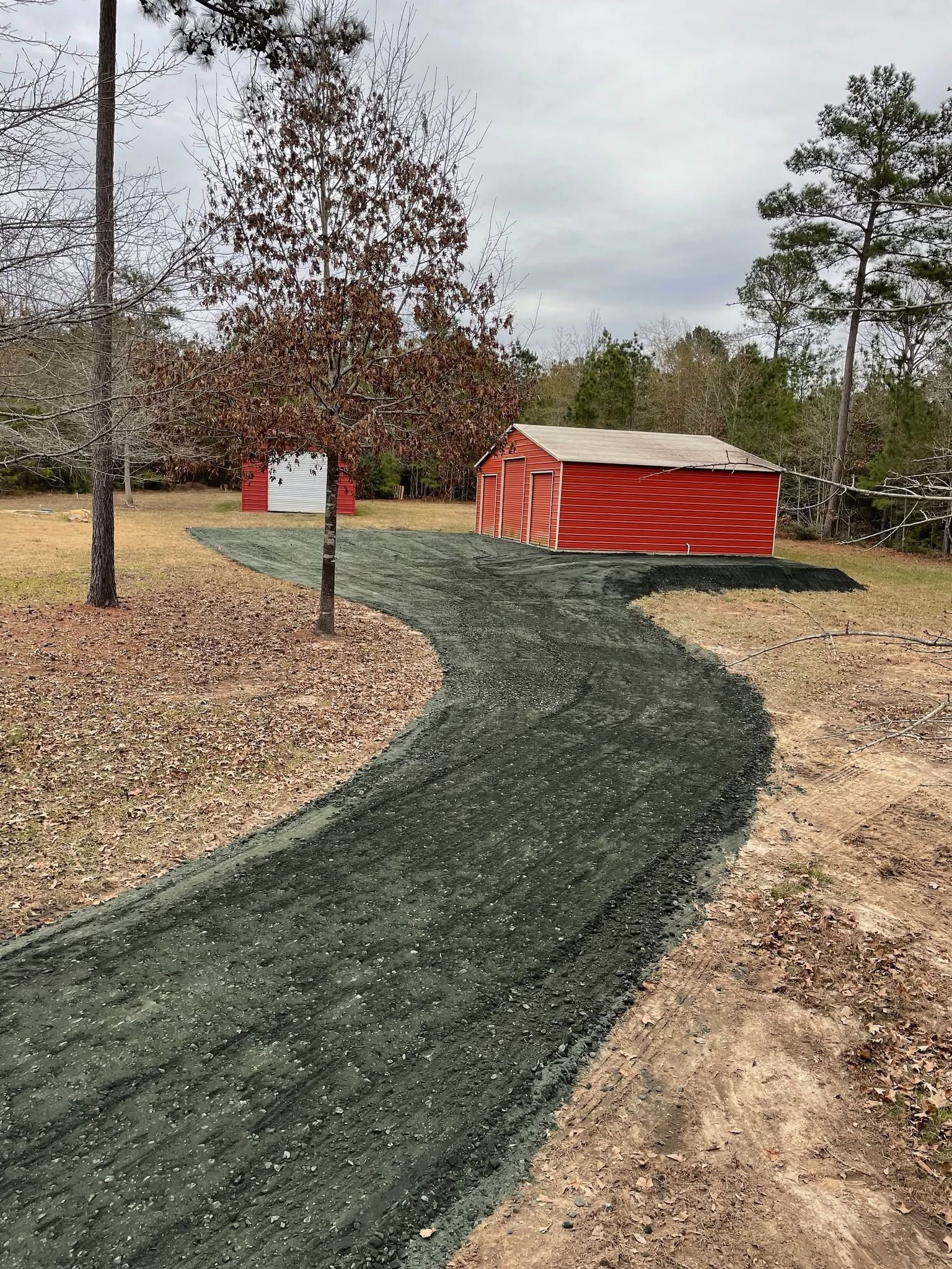 Curved gravel path through an outdoor campsite with red cabins and bare trees under a cloudy sky