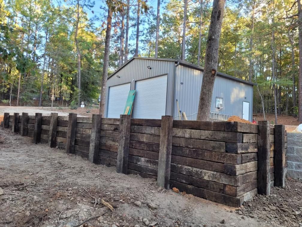 Outdoor shed behind a dark timber retaining wall in a wooded area