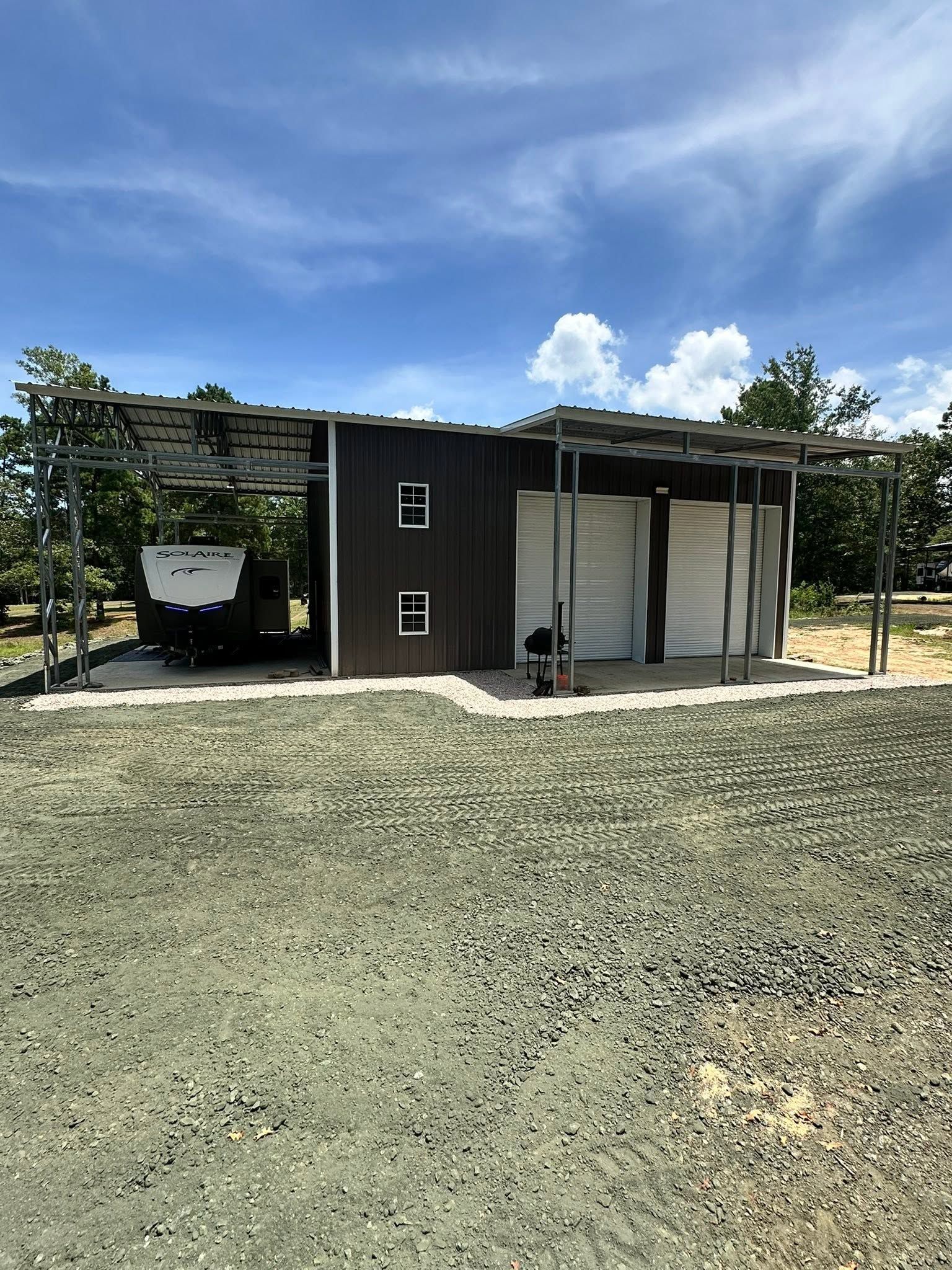 Small black-and-white utility building with an open carport and gravel yard under a blue sky.