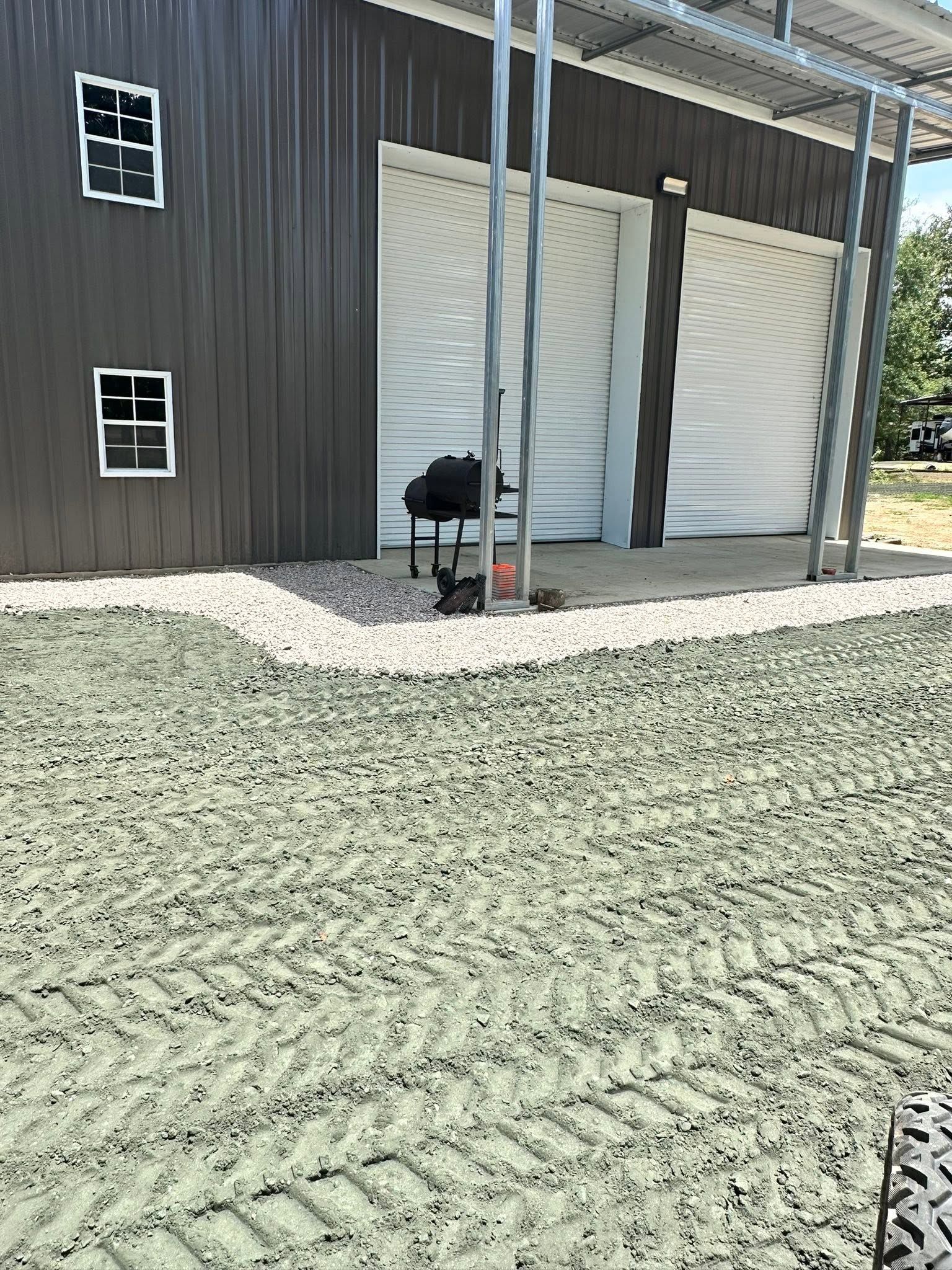 Barn exterior with dark siding, white garage door, and gravel driveway under a covered porch
