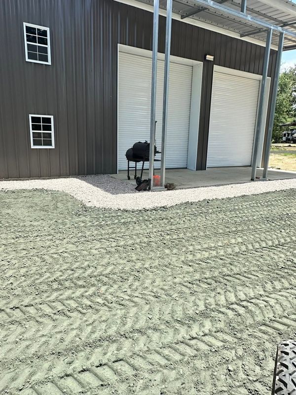 Barn exterior with dark siding, white garage door, and gravel driveway under a covered porch