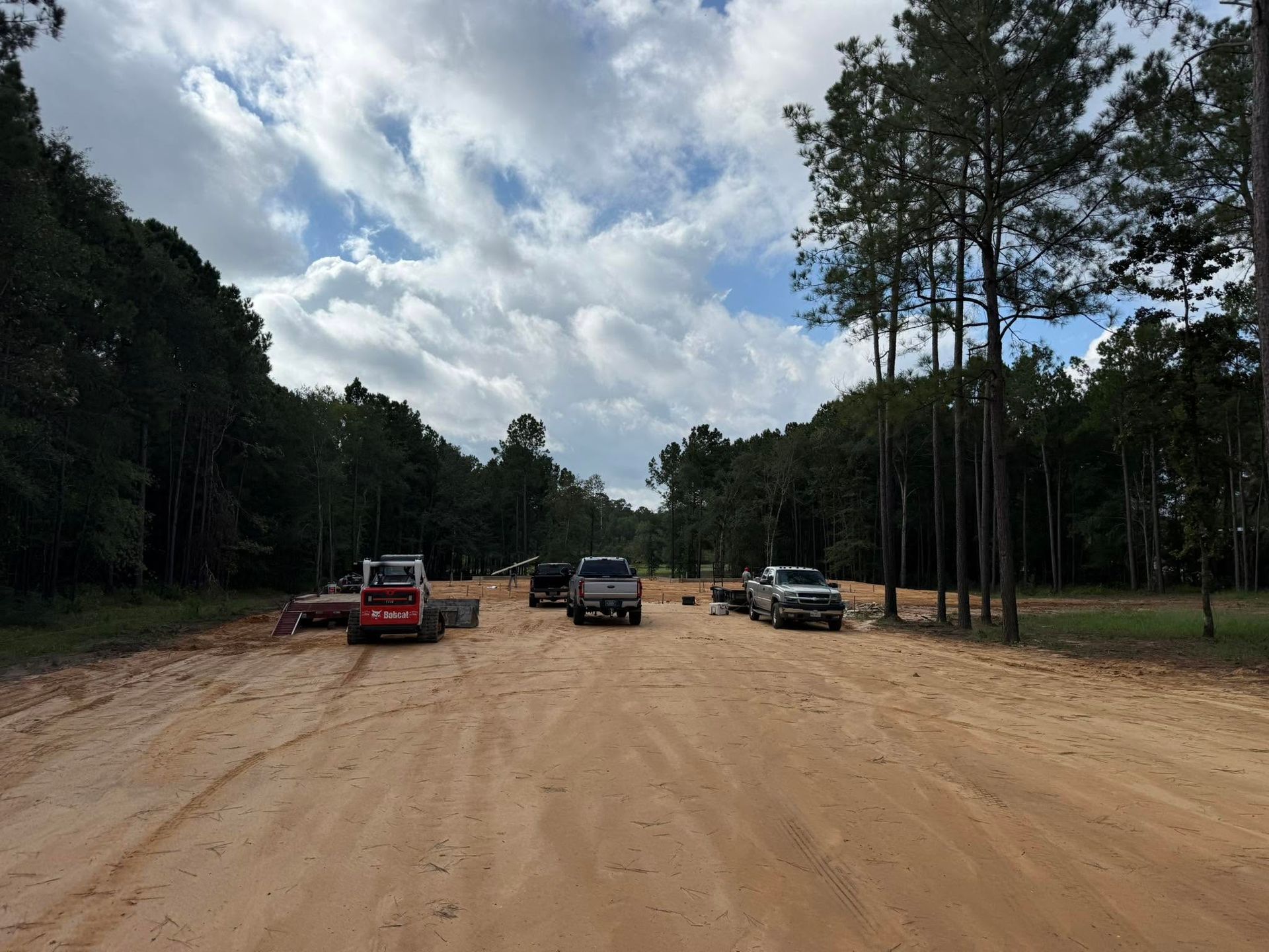 Several vehicles parked on a sandy dirt road beside a forest under a cloudy sky