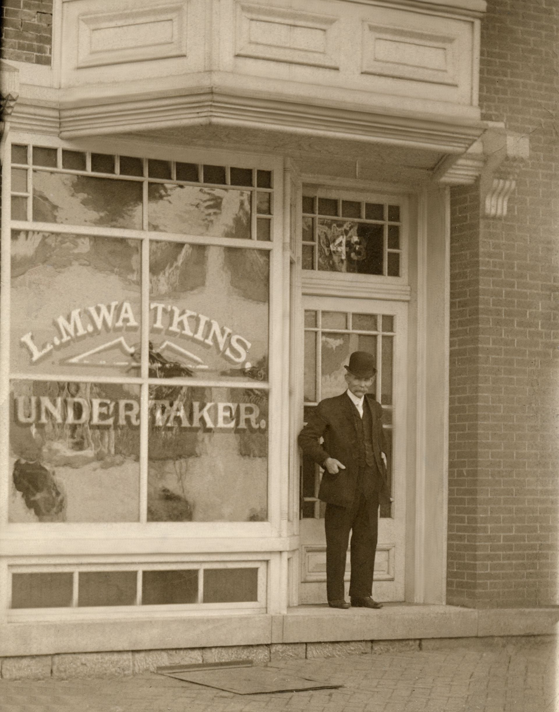 Man in a suit stands outside a storefront window,
