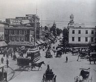 Busy street scene with horse-drawn carriages, streetcars, buildings, and pedestrians.